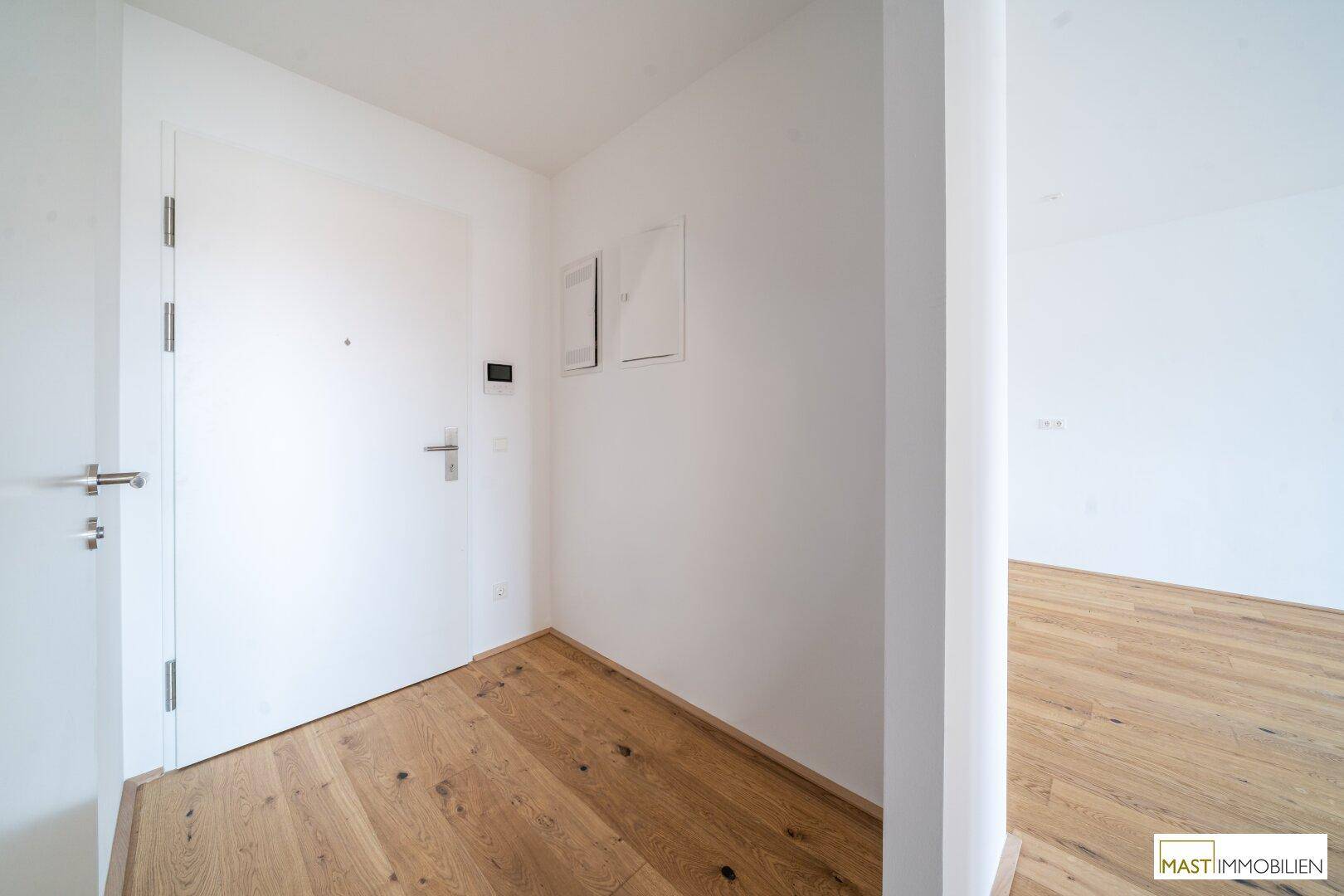 Heller Eingangsbereich mit Holzboden und weißer Wohnungstür, einladend gestaltet.