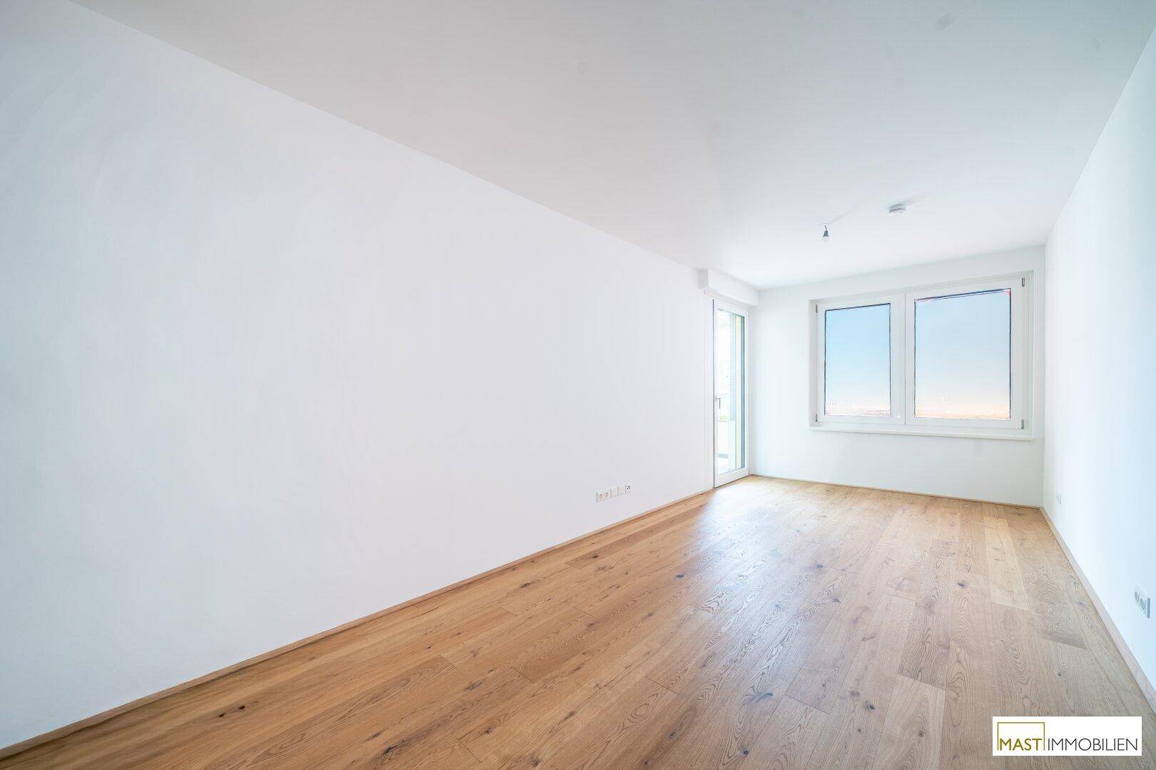 Helles, leeres Zimmer mit Holzboden und großen Fenstern, ideal als Schlaf- oder Arbeitszimmer.