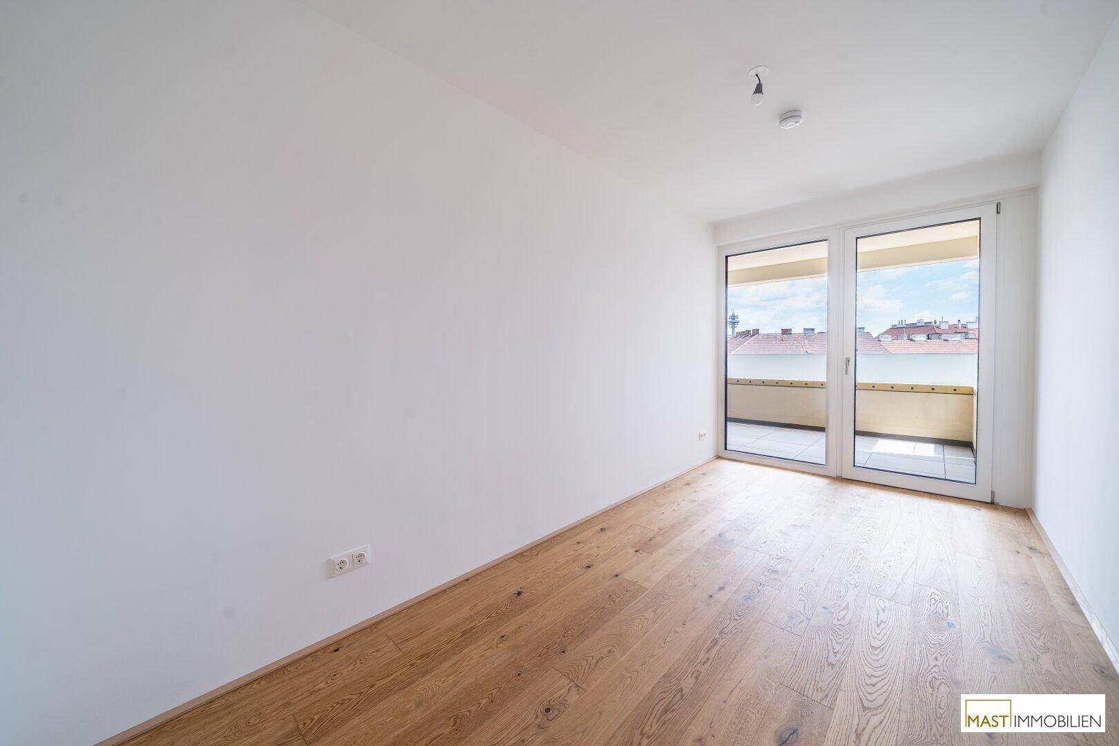 Leeres Schlafzimmer mit Holzboden und direktem Zugang zu einem sonnigen Balkon.