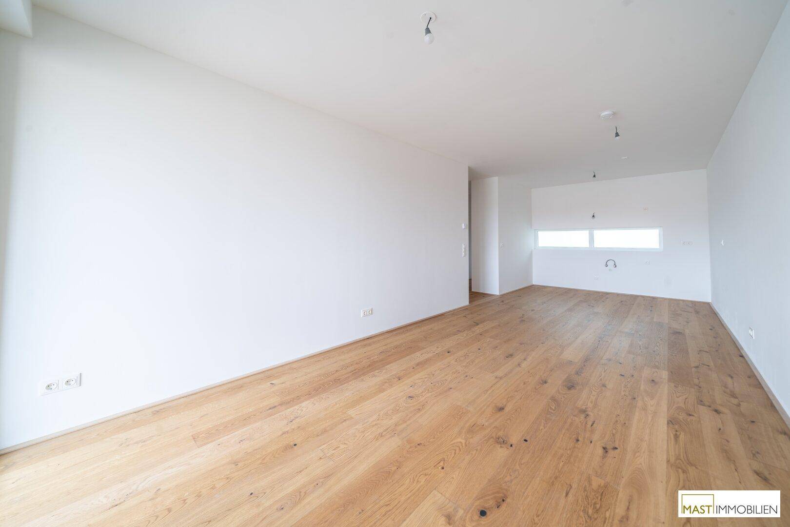 Heller, leerer Raum mit Holzboden, vorgesehen für eine Küche, mit Fenster.