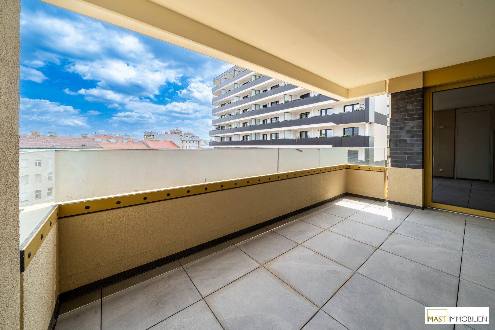 Geräumiger Balkon mit Fliesenboden und Blick auf umliegende Gebäude, ideal zum Entspannen.