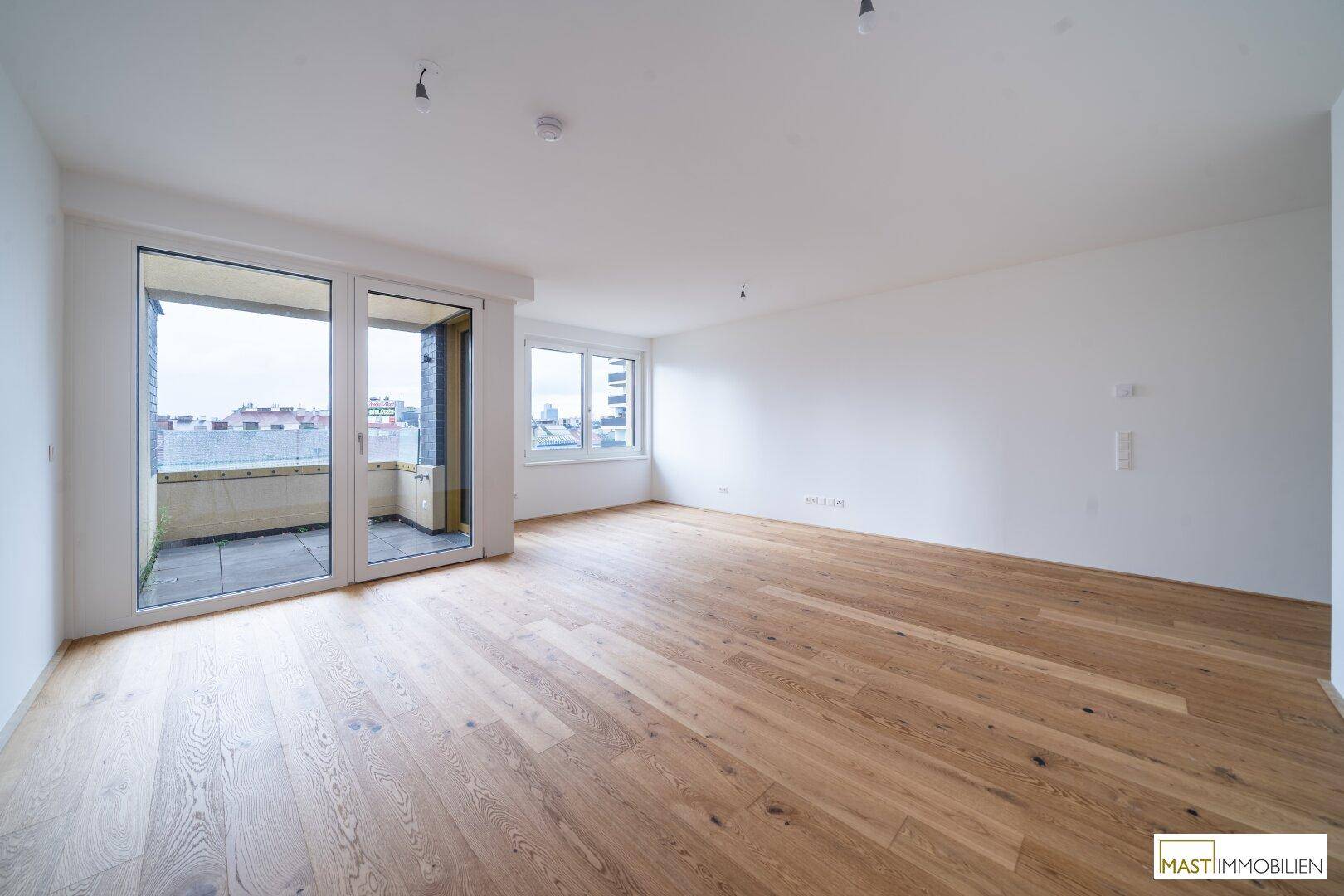 Geräumiger, heller Wohnbereich mit Holzboden und großem Balkonzugang mit Stadtblick.