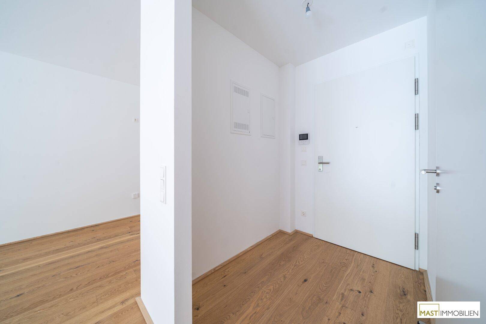 Eingangsbereich mit Eichenparkettboden, weißer Wand und moderner Gegensprechanlage.
