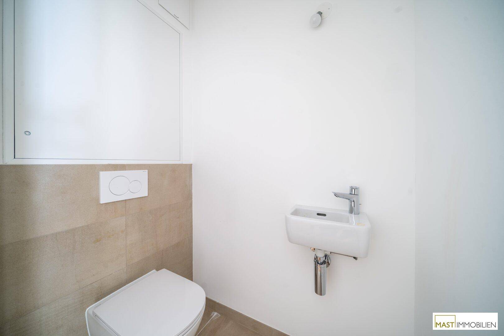 Modernes Gäste-WC mit wandhängender Toilette, kleinem Waschbecken und beigefarbenen Fliesen.