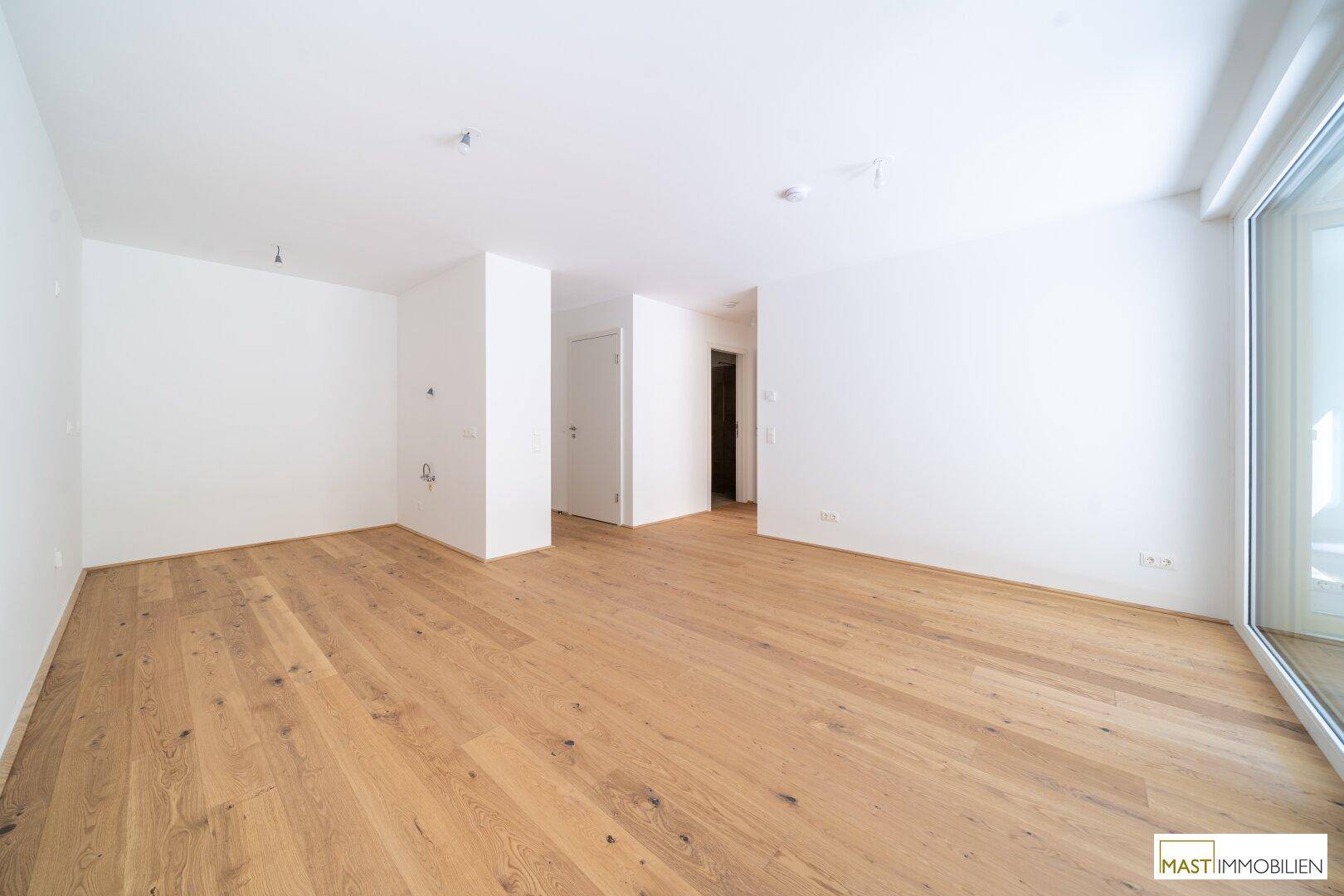 Helles, leeres Zimmer mit Eichenparkettboden und großem Fenster mit Zugang nach draußen.