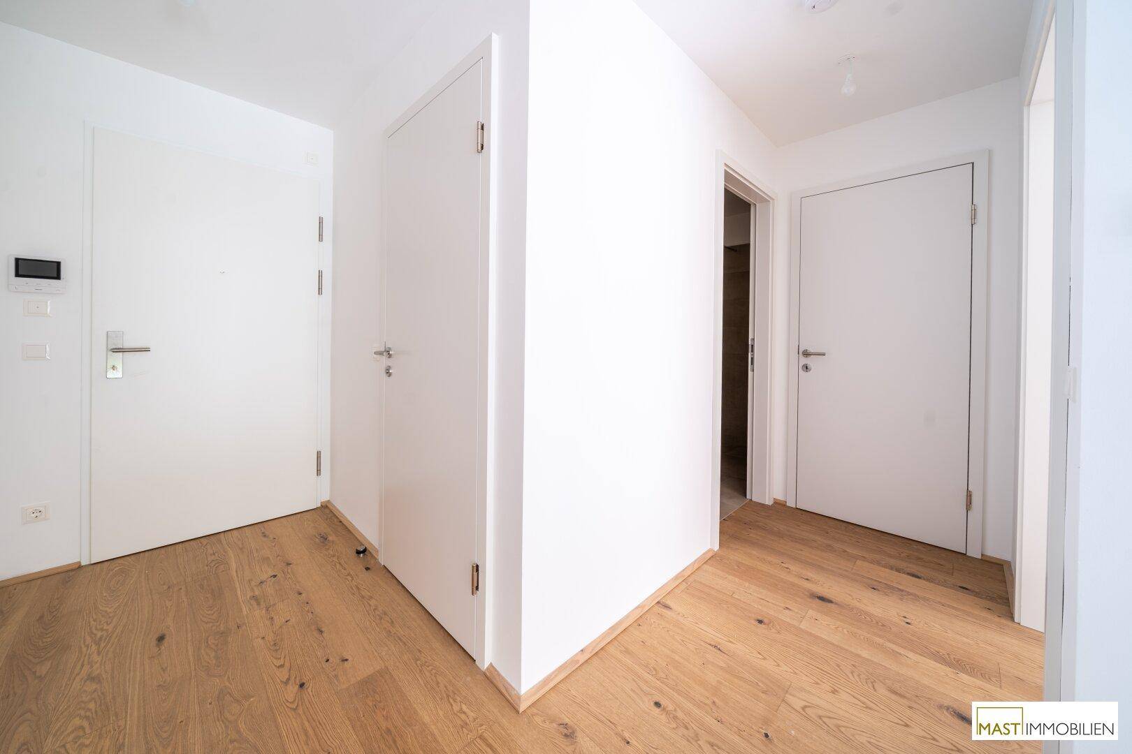 Heller Flur mit Eichenparkettboden und mehreren weißen Türen, die zu verschiedenen Räumen führen.