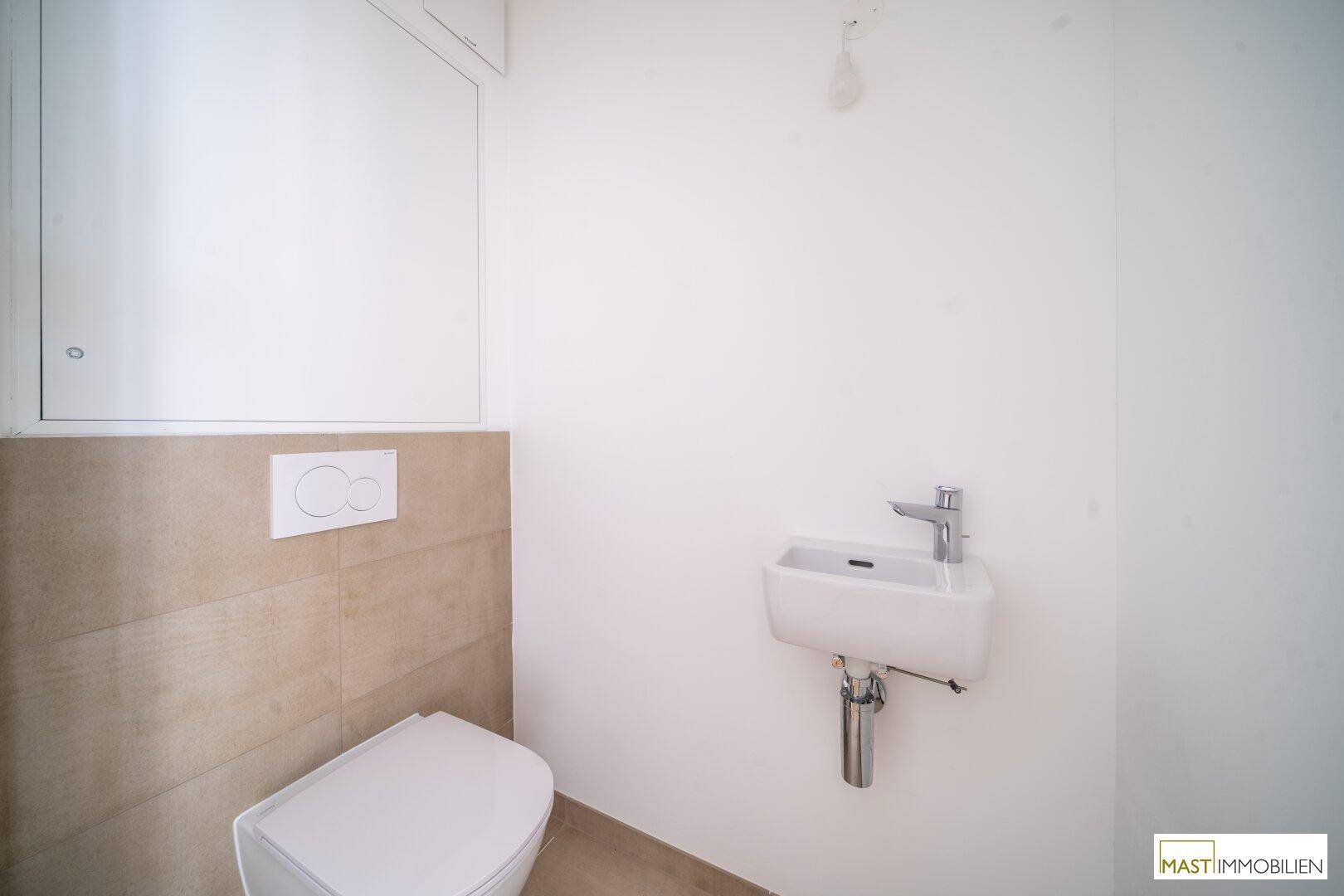 Modernes Gäste-WC mit wandhängendem WC, kleinem Waschbecken und beigefarbenen Fliesen.