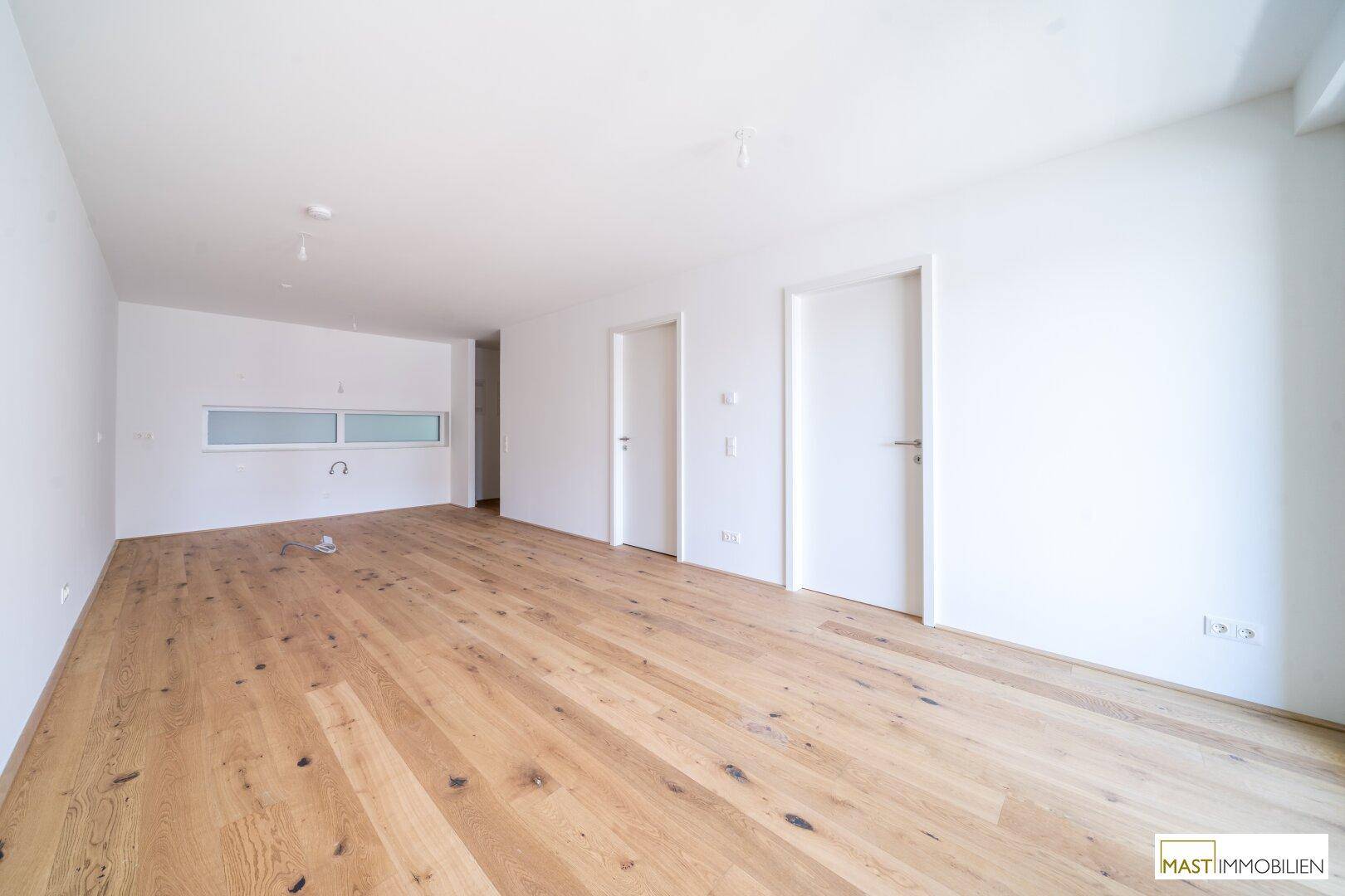 Helles, leeres Zimmer mit modernem Holzboden und weißen Wänden, bereit zur individuellen Gestaltung.