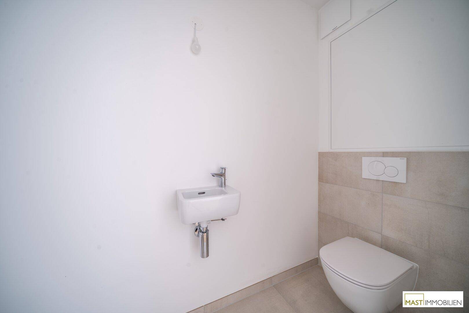 Modernes Gäste-WC mit wandhängender Toilette und kleinem Waschbecken in hellen Farbtönen.