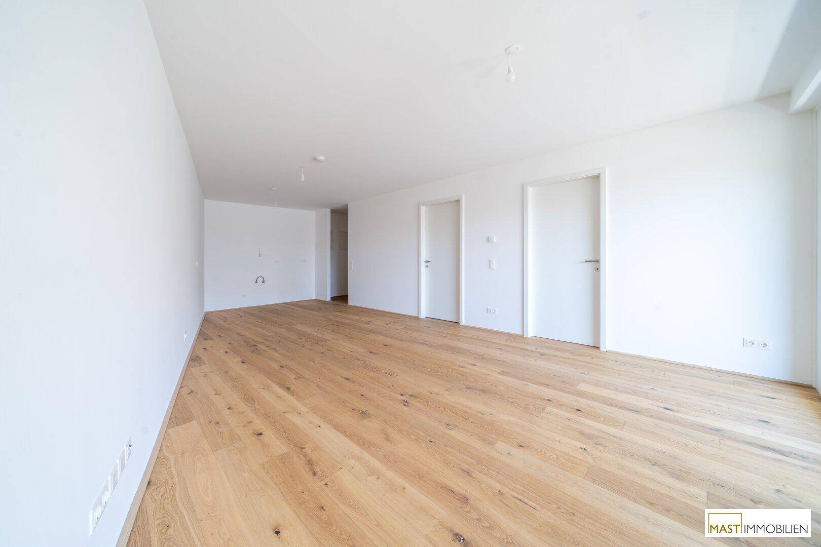 Helles, leeres Zimmer mit neuem Holzboden und weißen Wänden, bereit für die Einrichtung.
