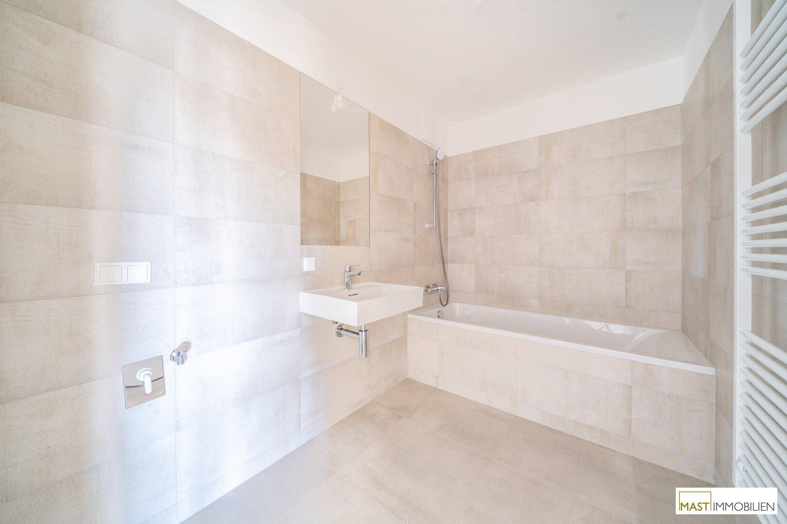 Modernes Badezimmer mit Badewanne, Waschbecken und beheiztem Handtuchhalter in hellen Fliesen.