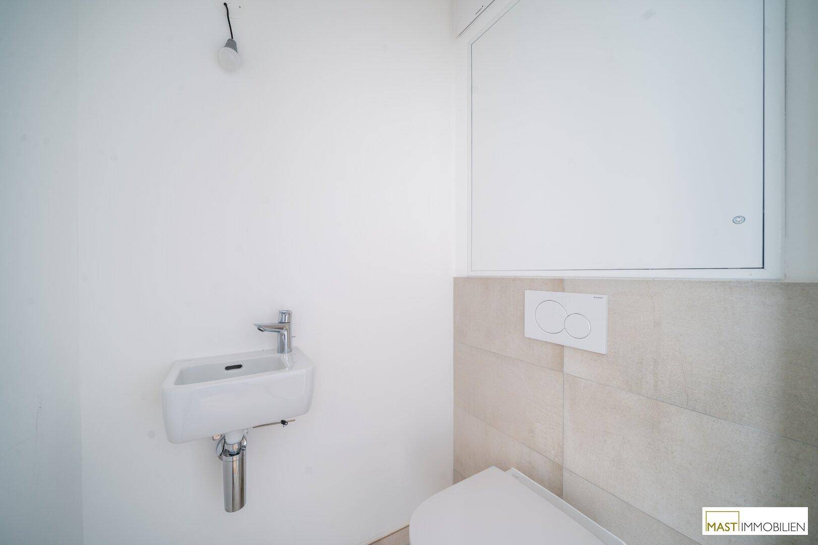 Modernes Gäste-WC mit Wand-WC, kleinem Waschbecken und hellen Fliesen.