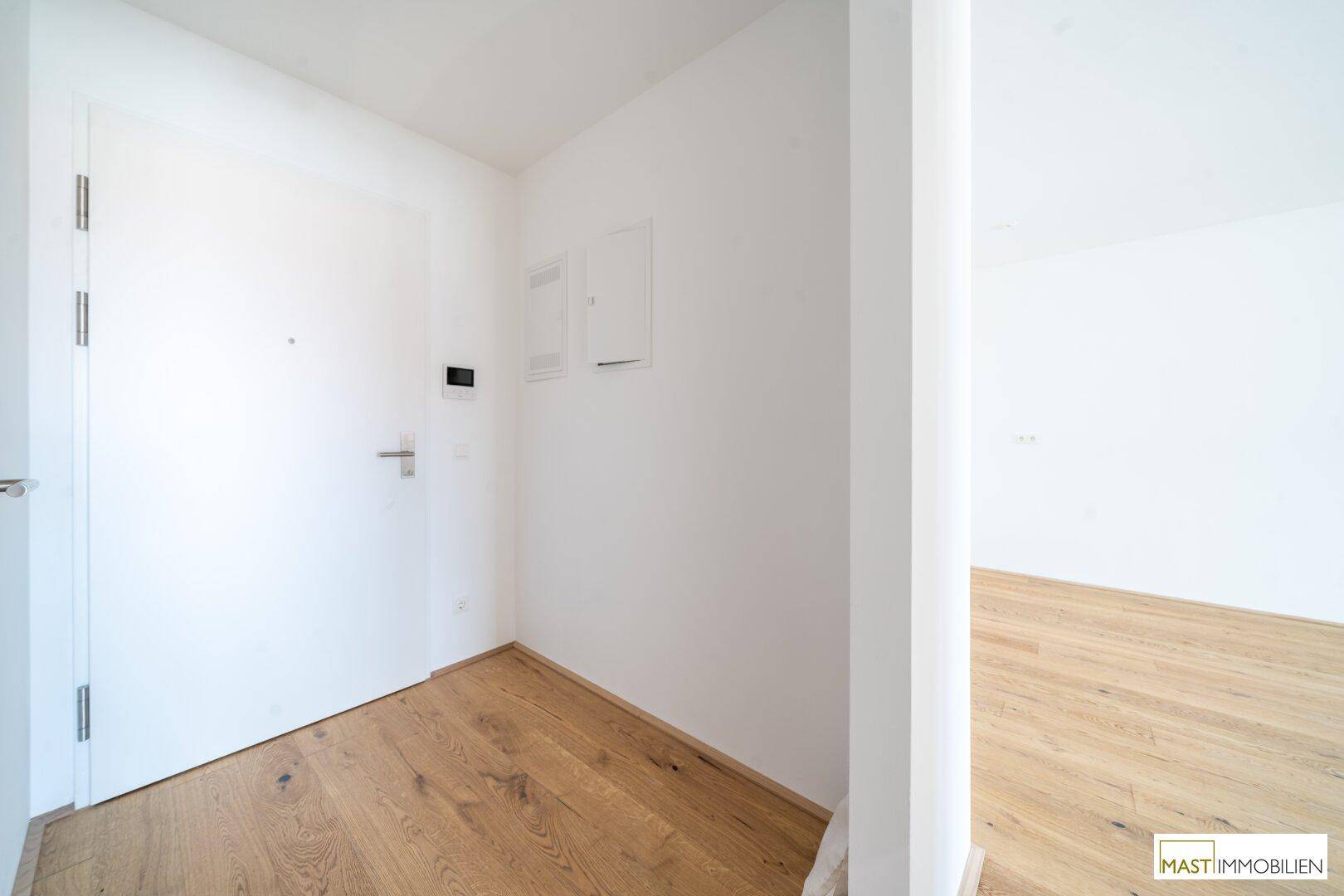 Heller Eingangsbereich mit Holzboden und weißer Tür, der zu den Wohnräumen führt.