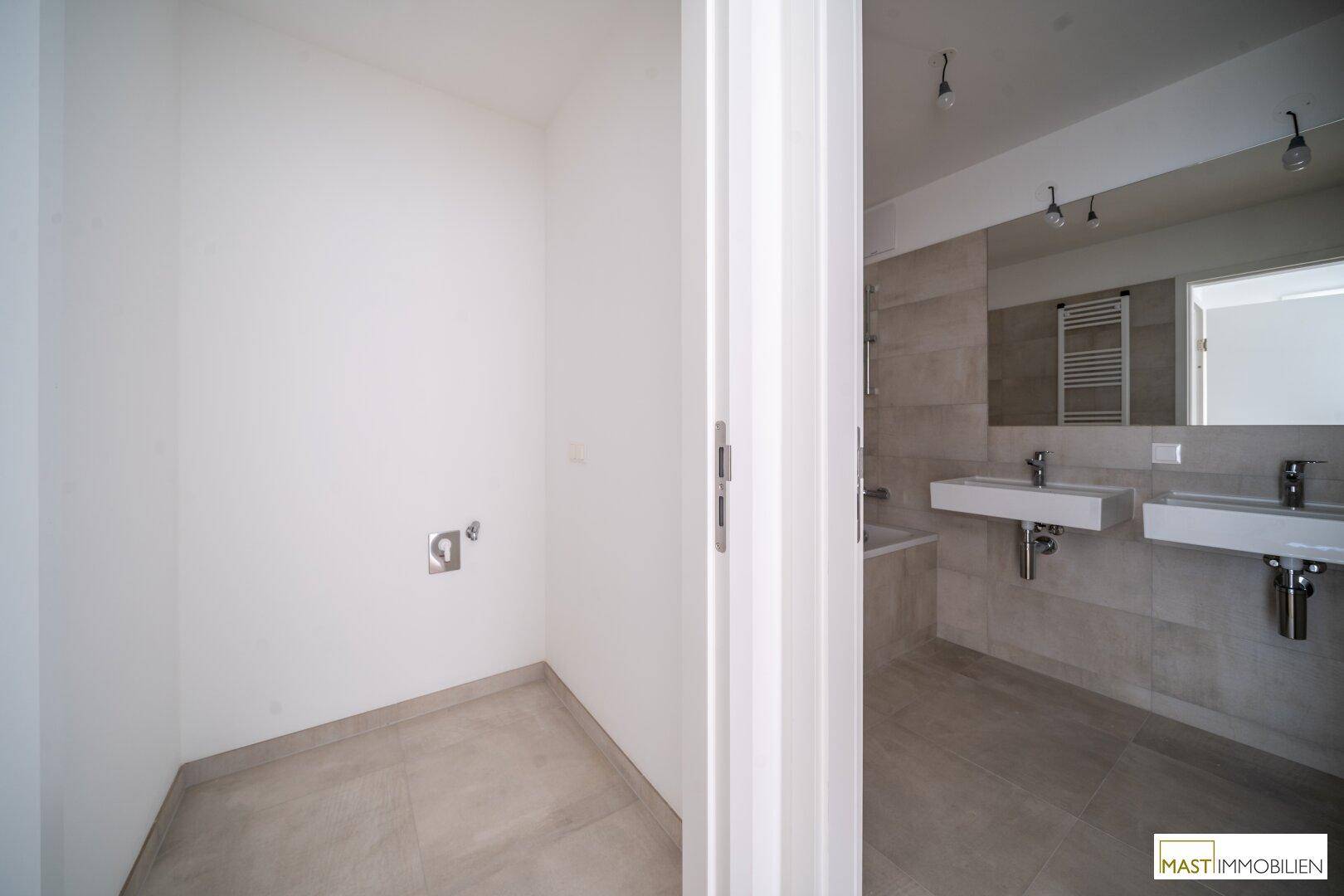 Praktischer Hauswirtschaftsraum mit Fliesenboden, angrenzend an ein modernes Badezimmer.
