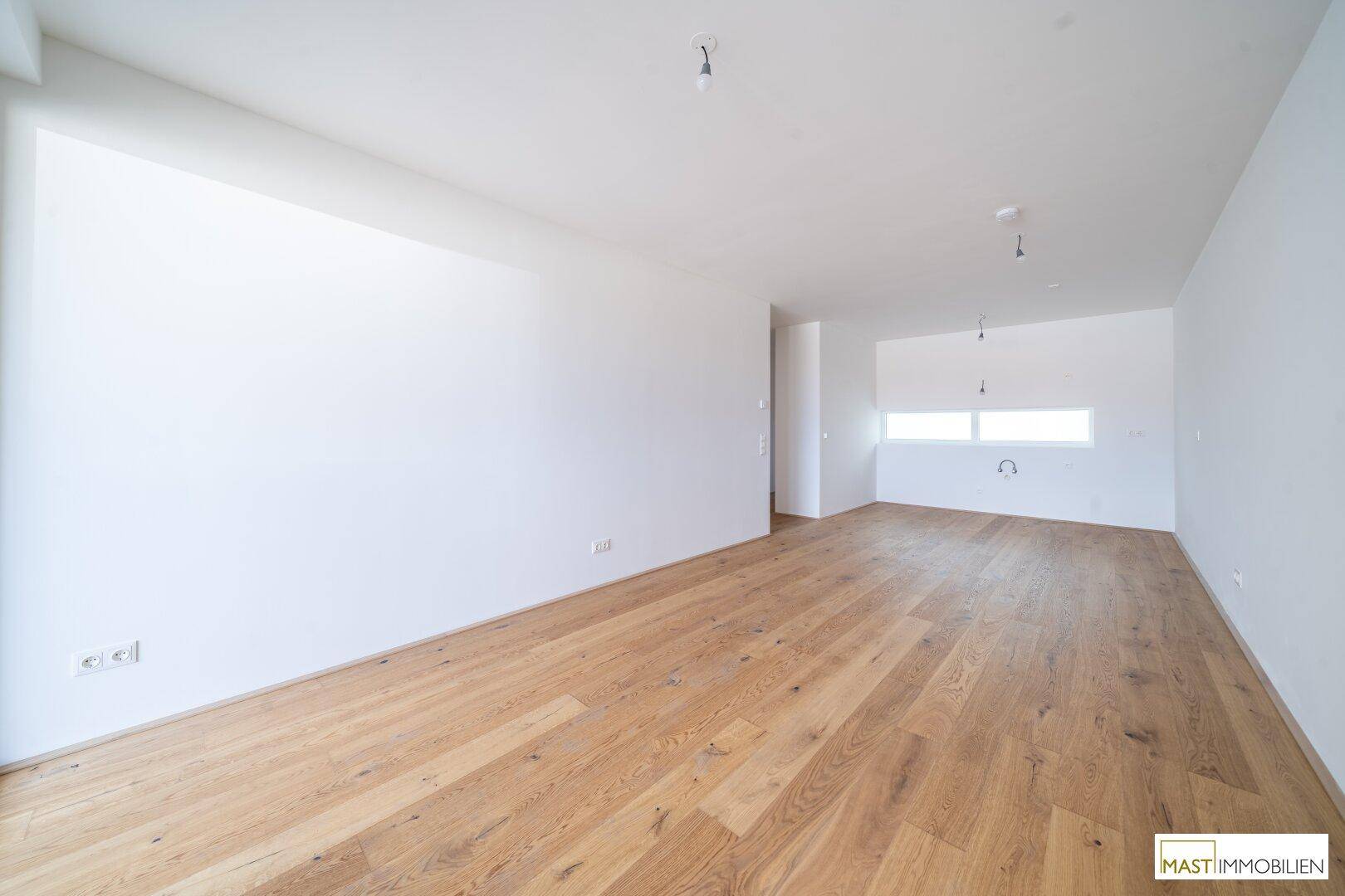 Geräumiges, helles Wohnzimmer mit Holzboden und großen Fenstern für viel Tageslicht.