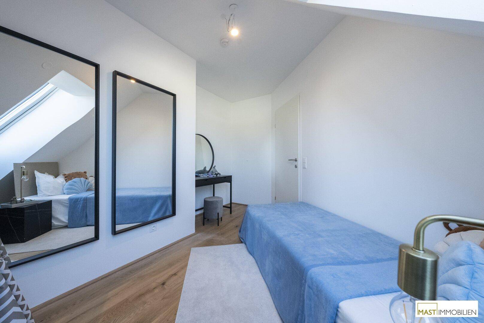 Helles Schlafzimmer mit Holzboden, großem Spiegel und modernem Dekor unter schrägen Decken.