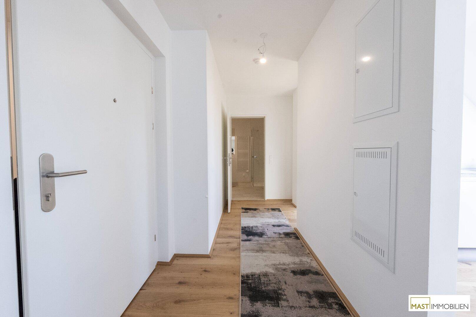 Heller Flur mit Holzboden und weiß gestrichenen Wänden, der zu den verschiedenen Räumen führt.