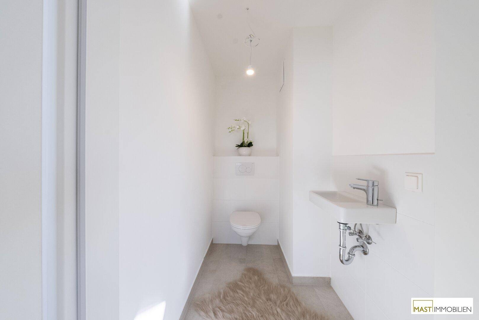 Modernes Gäste-WC mit Wand-WC, kleinem Waschbecken und Fliesenboden in hellem Design.