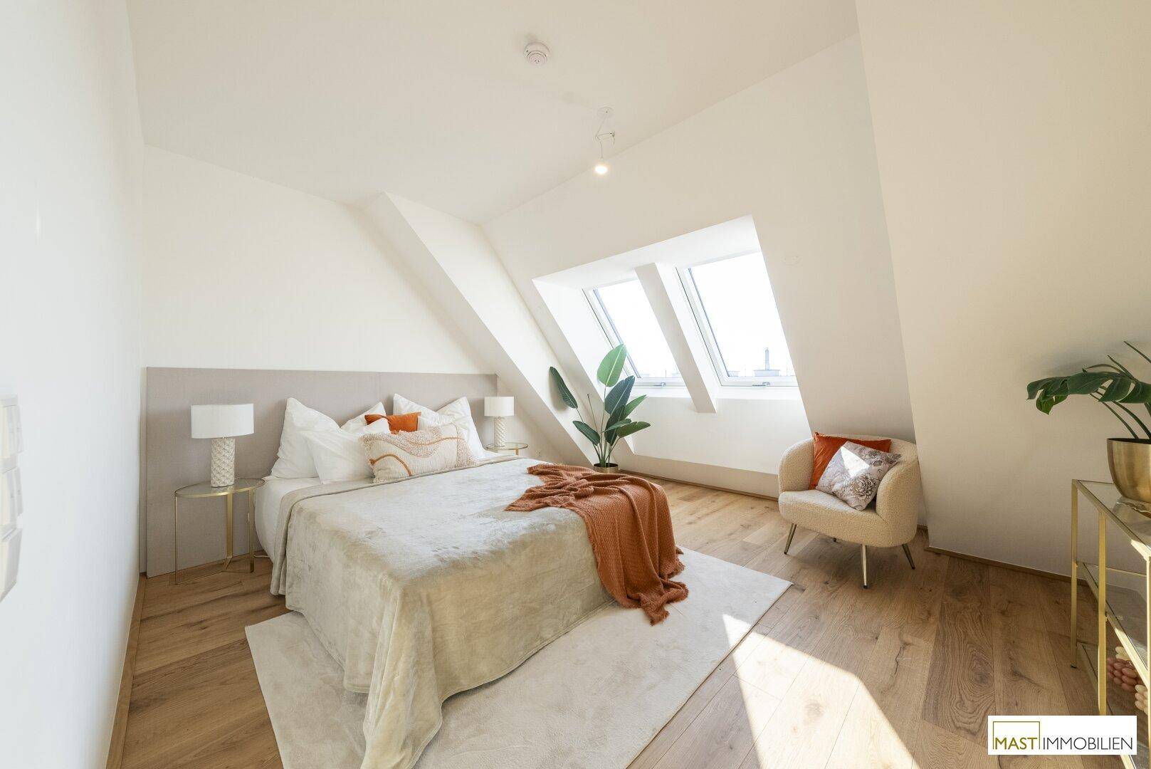 Helles Schlafzimmer mit großem Bett, Holzboden und Dachfenstern, die viel Tageslicht hereinlassen.