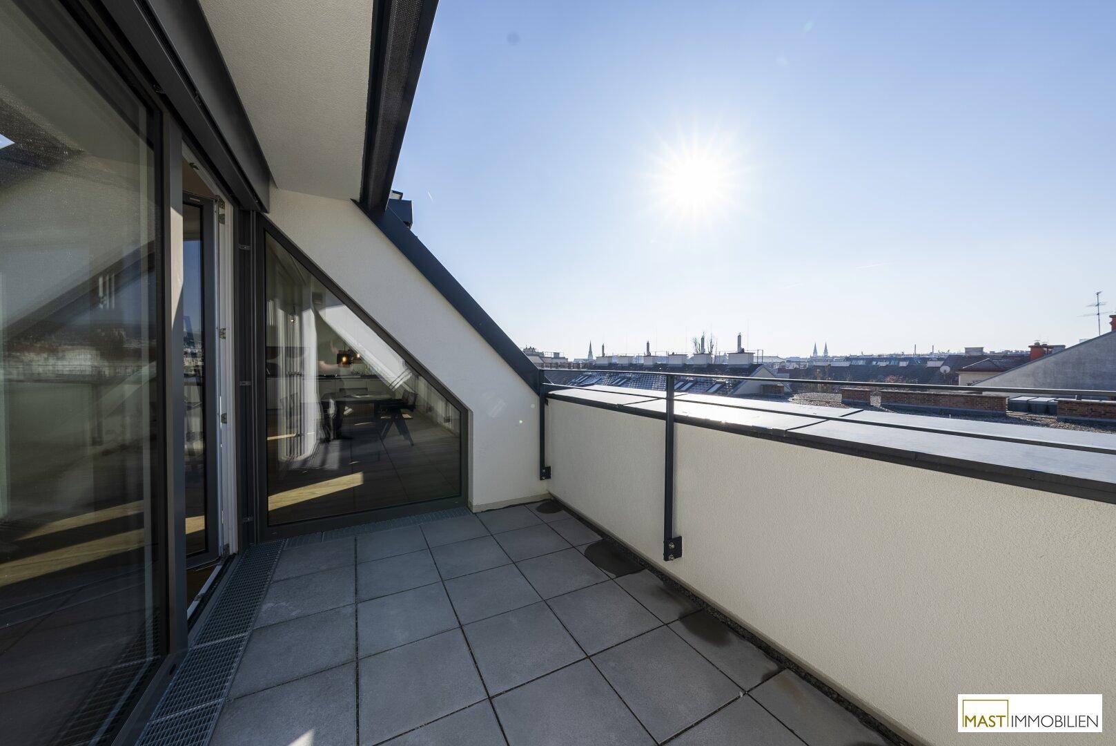 Sonnige Dachterrasse mit Fliesenboden und weitem Blick über die Stadt und die Dächer Wiens.