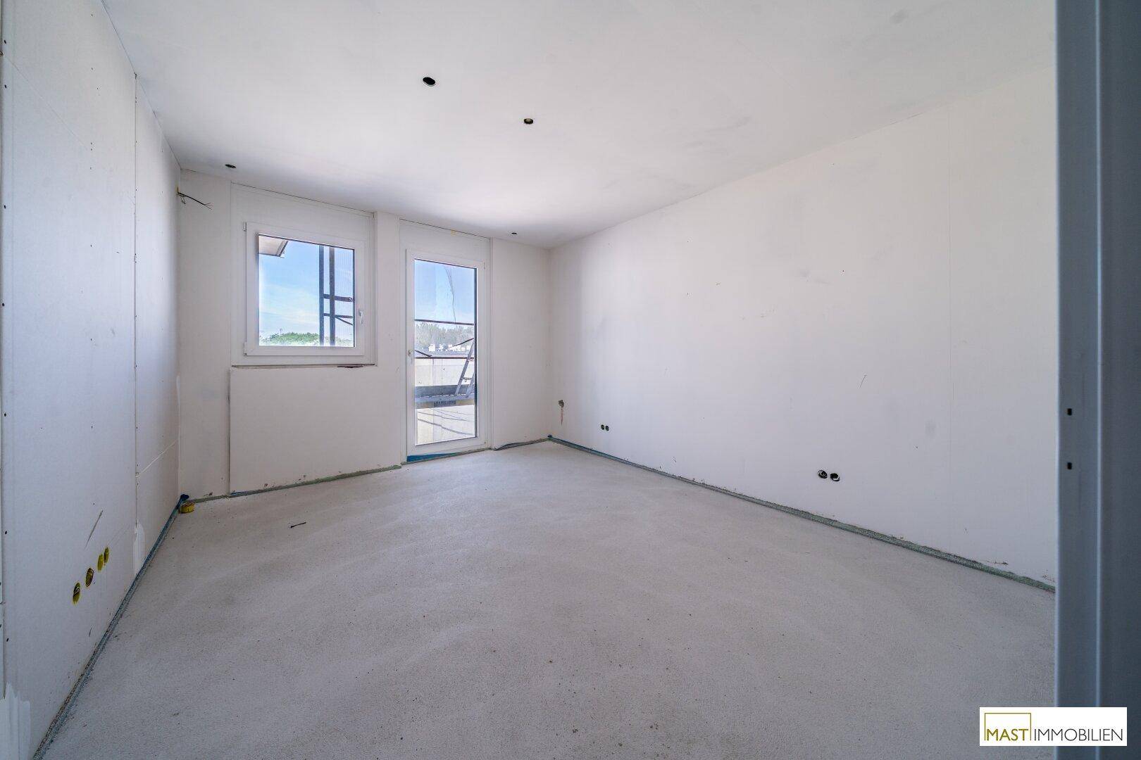 Helles, unfertiges Zimmer mit zwei Fenstern und Zugang zu einem Außenbereich, ideal für ein Schlafzimmer.