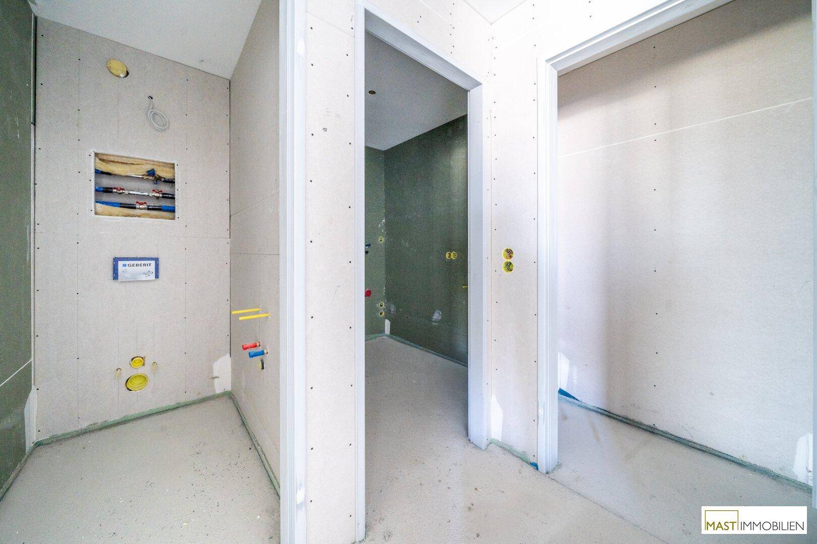 Unfertiges Badezimmer mit Trockenbauwänden und sichtbaren Sanitärinstallationen, im Rohbau.
