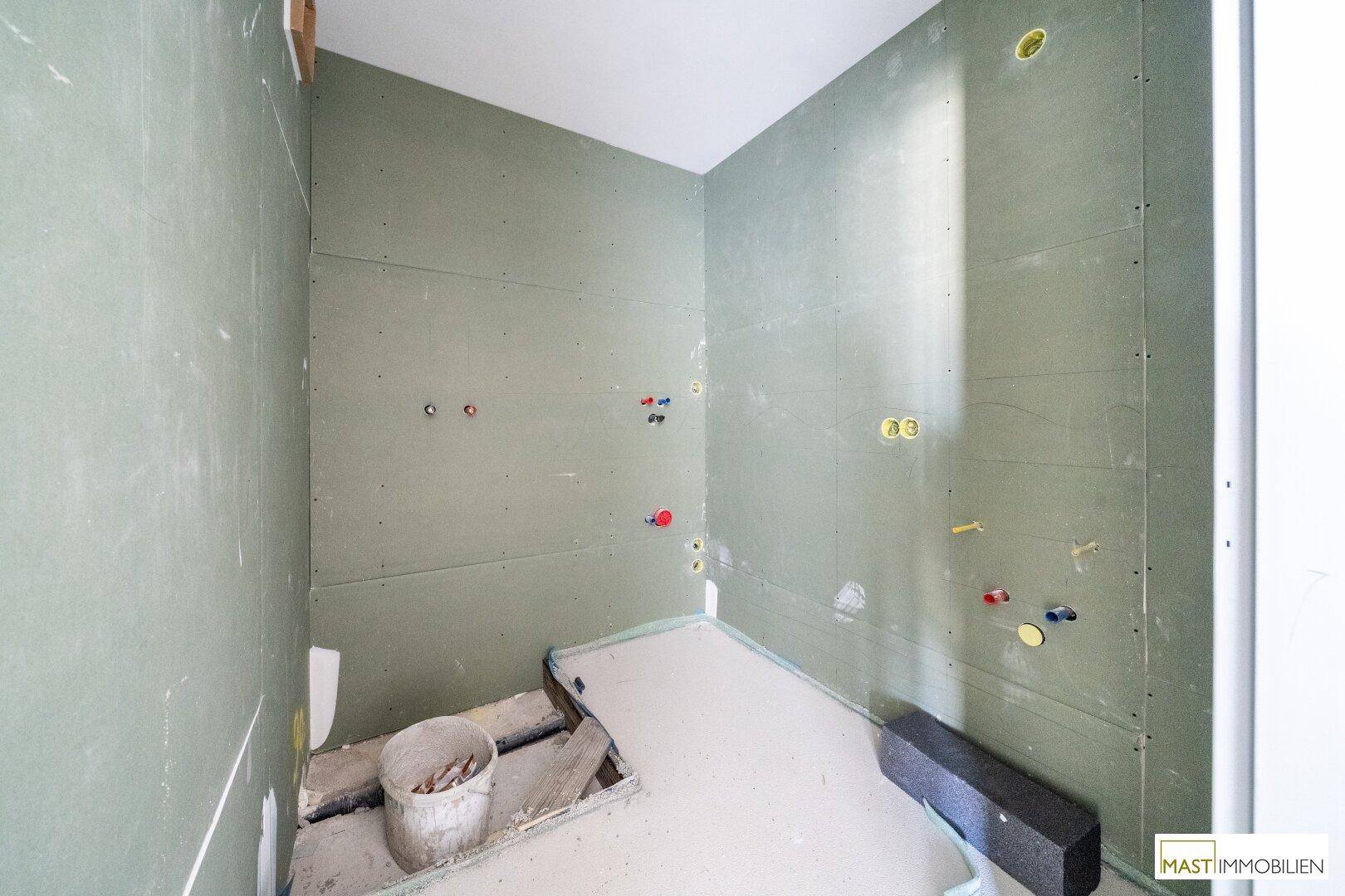 Detailansicht eines unfertigen Badezimmers mit grünen Trockenbauwänden und sichtbaren Leitungen.