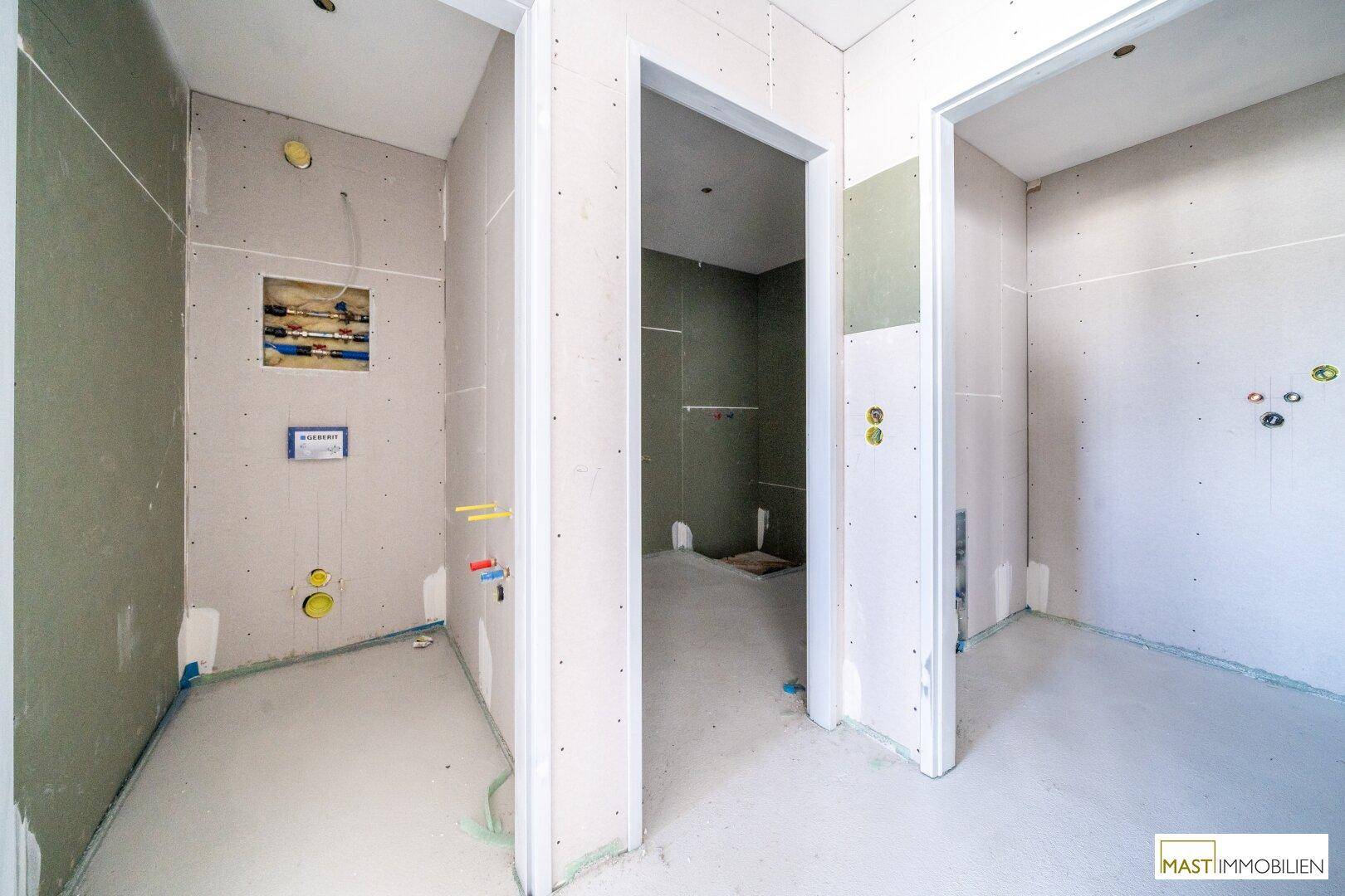 Unfertiges Badezimmer mit vorbereiteten Anschlüssen für Dusche, Toilette und Waschbecken.