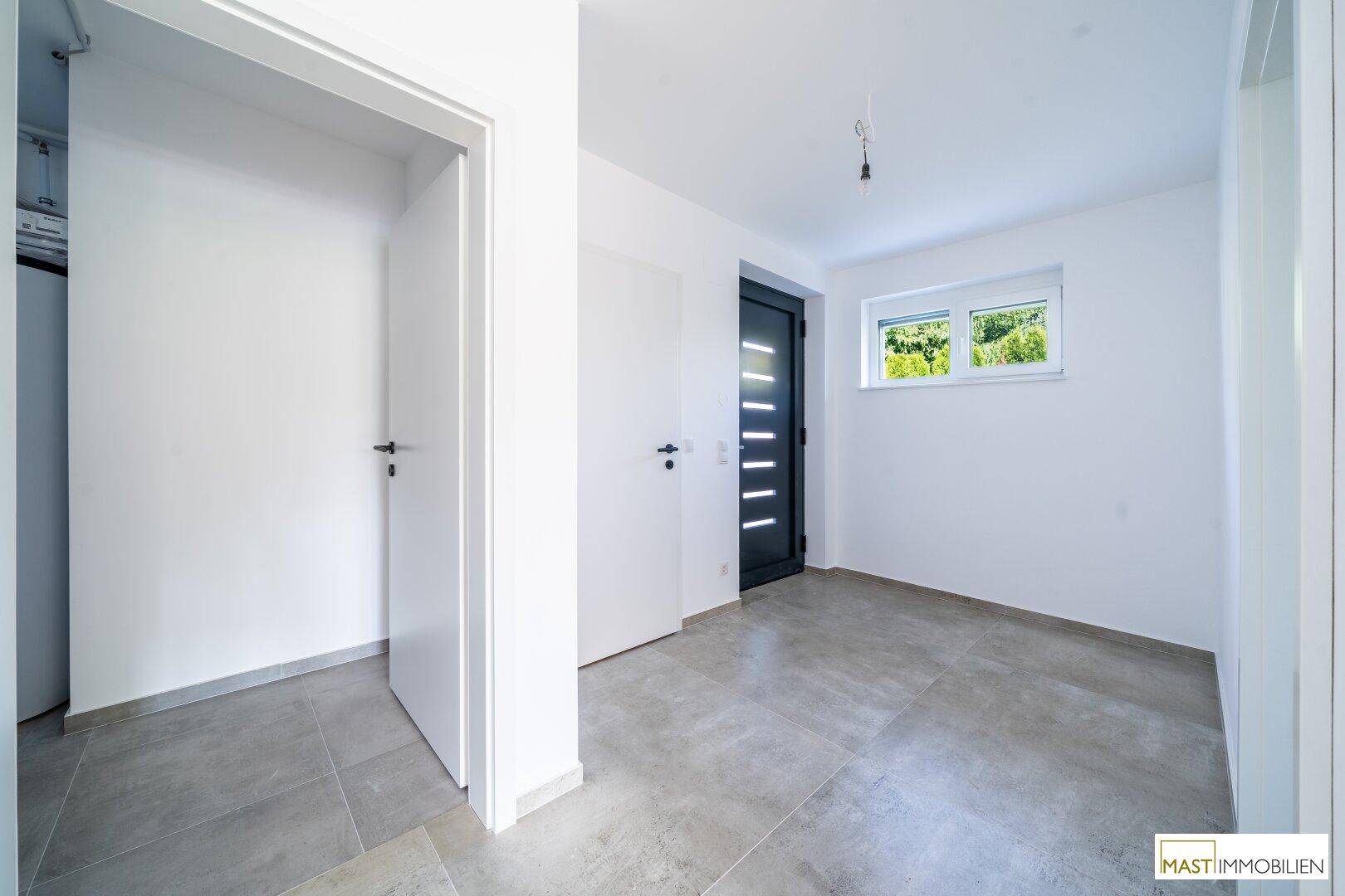 Moderner Eingangsbereich mit grauen Fliesen, weißer Tür und Fenster für natürliches Licht.