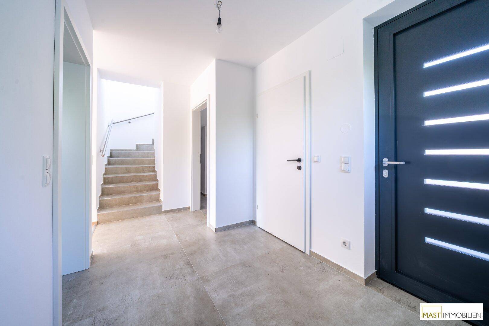 Heller Flur mit grauen Fliesen, moderner Eingangstür und Treppe zum Obergeschoss.