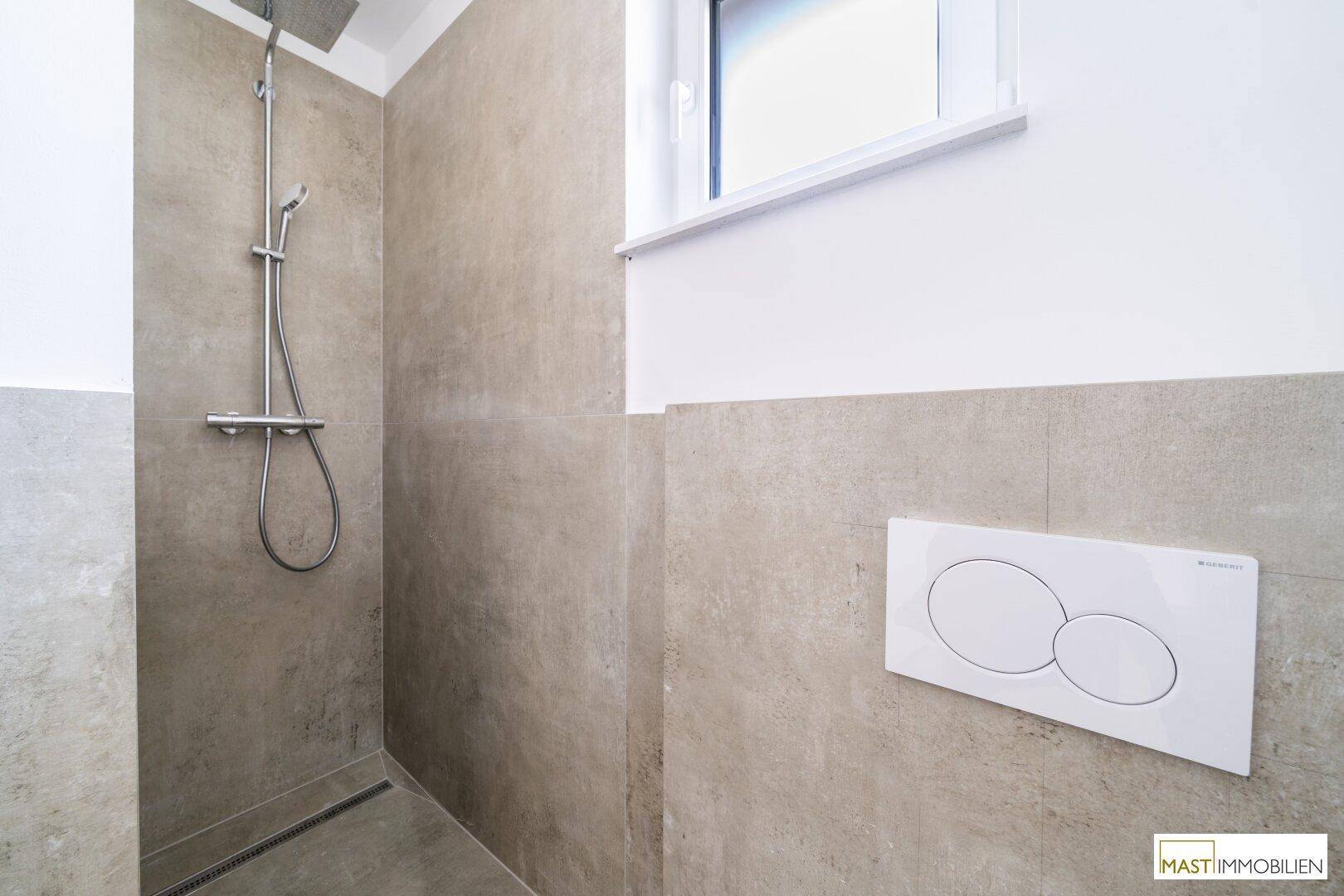 Moderne Dusche mit grauen Fliesen, Duschkopf und Fenster für gute Belüftung.