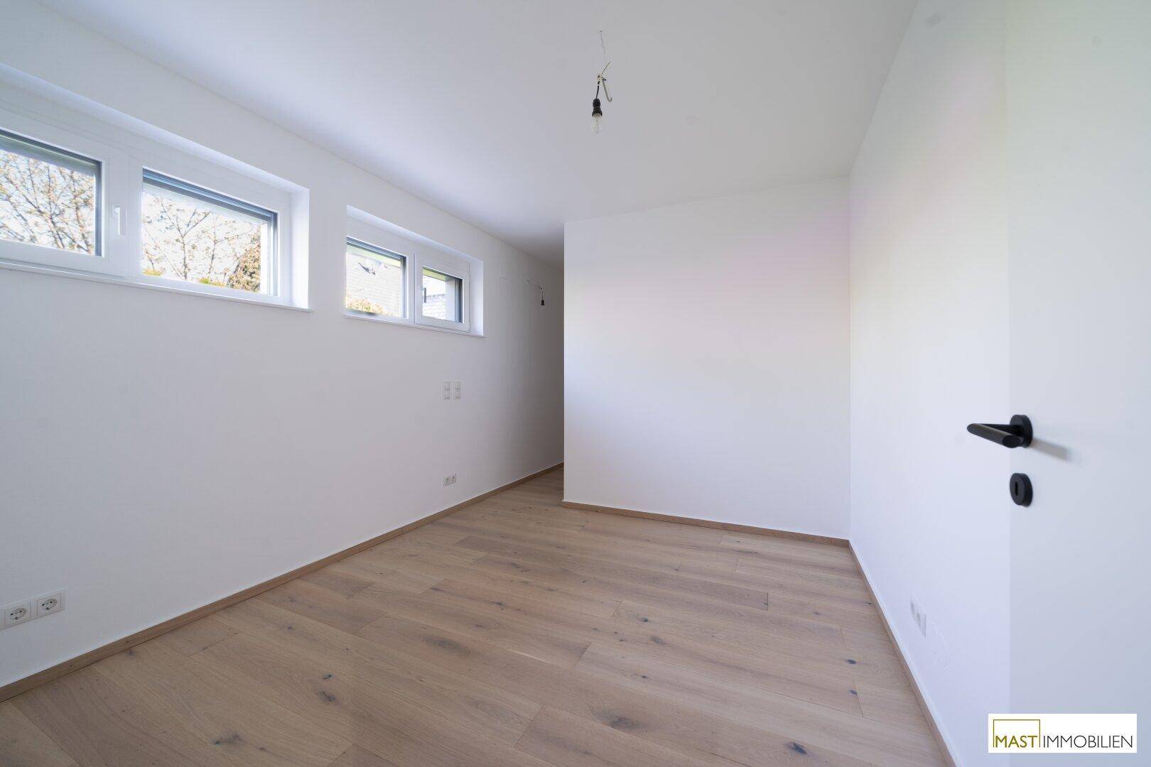 Helles Zimmer mit Holzboden und drei Fenstern, ideal als Schlaf- oder Arbeitszimmer.