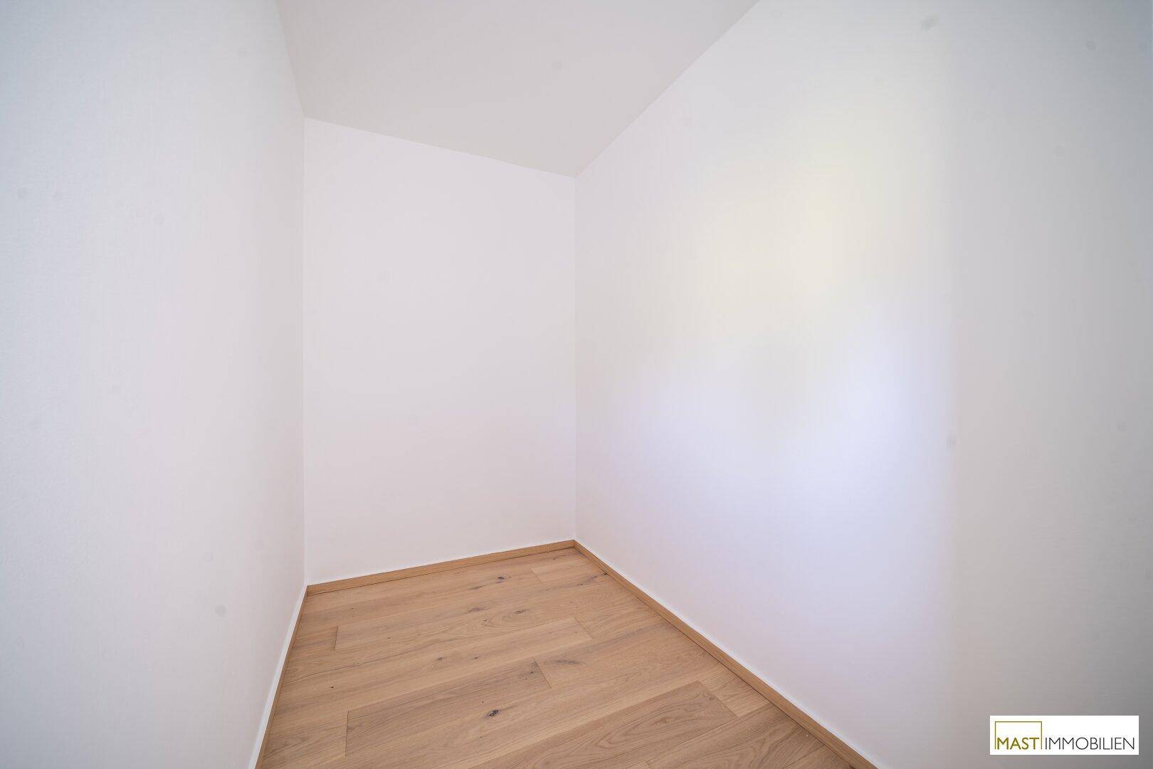 Kleiner, heller Raum mit Holzboden und weißen Wänden, ideal als Abstellraum oder Ankleidezimmer.