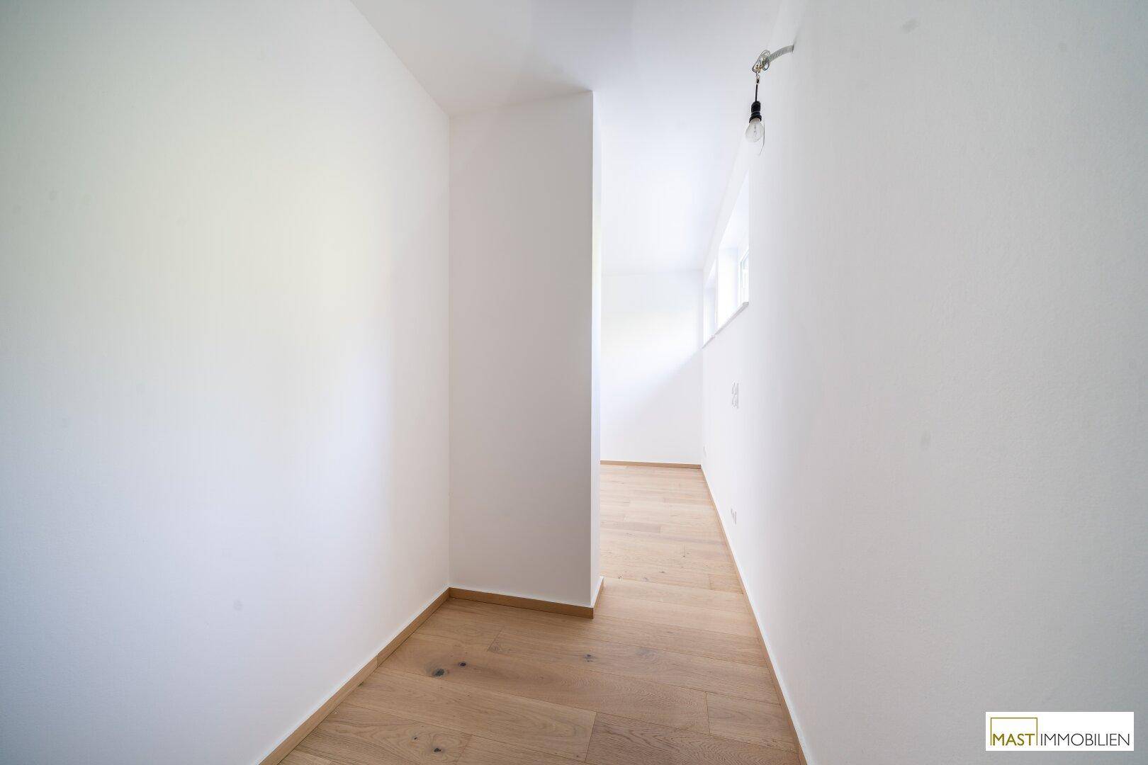 Schmaler, heller Flur mit Holzboden und weißen Wänden, der zu weiteren Räumen führt.