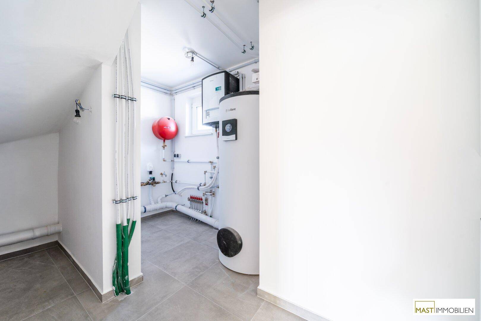 Technikraum mit Warmwasserspeicher und Installationen, ausgestattet mit Fliesenboden und Fenster.
