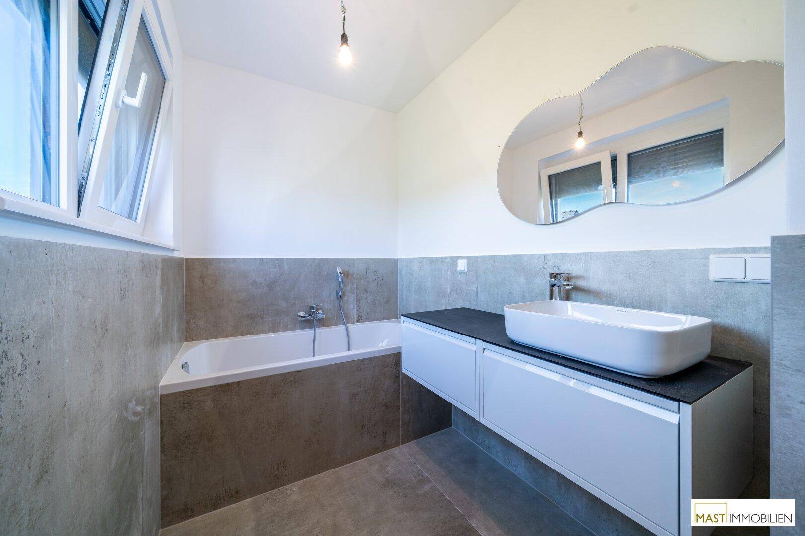 Modernes Badezimmer mit Badewanne, stilvollem Waschtisch und Fenster für natürliches Licht.
