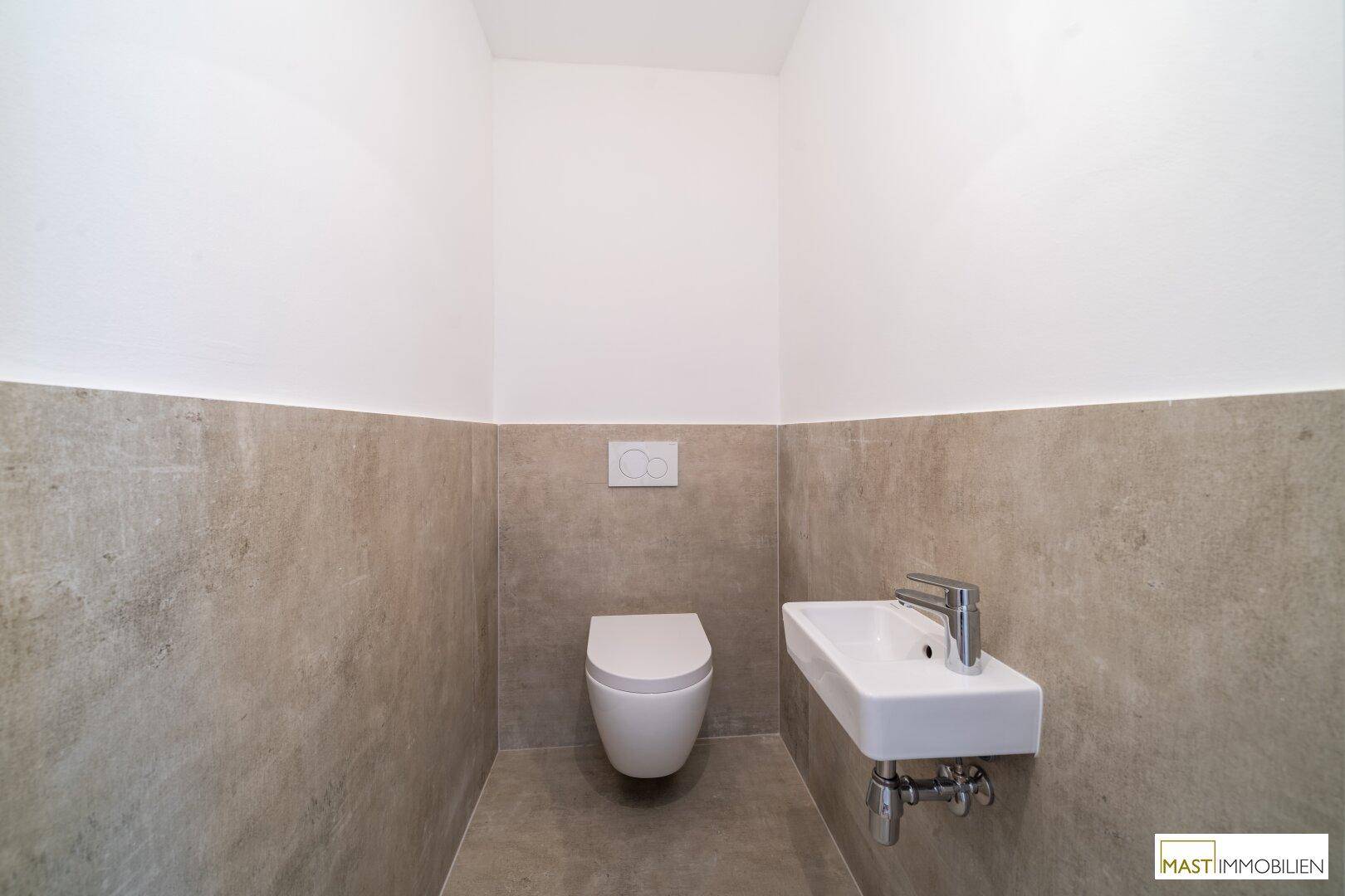 Modernes Gäste-WC mit wandhängender Toilette und kleinem Waschbecken in neutralen Farben.