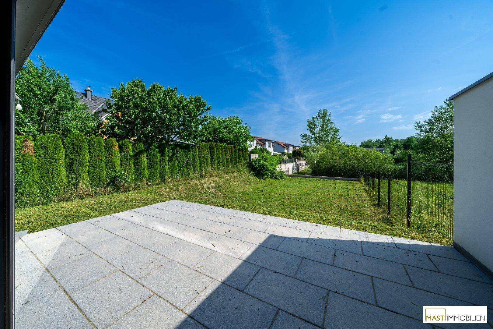 Geräumige Terrasse mit Steinplatten und direktem Zugang zu einem gepflegten Rasenbereich.