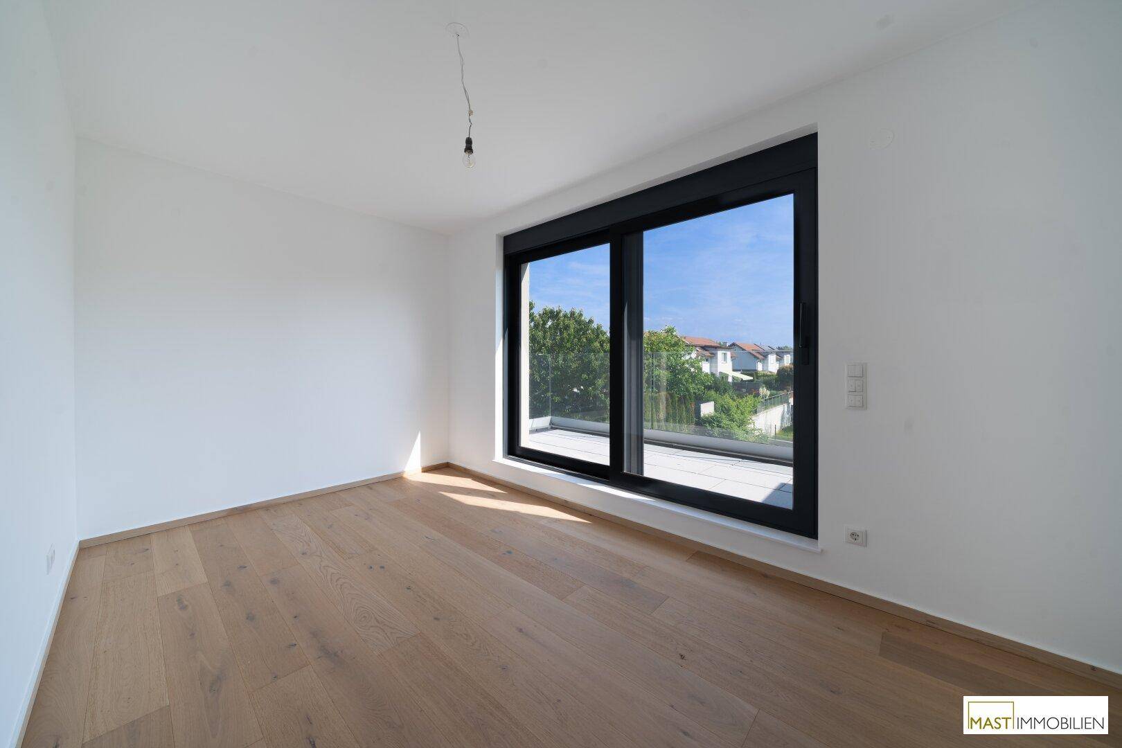 Helles Zimmer mit Holzboden und großem Fenster mit Blick auf die Umgebung.