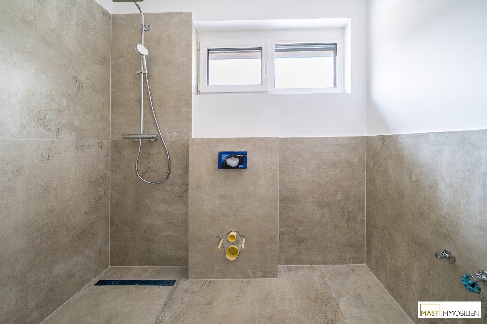 Modernes Badezimmer im Bau mit begehbarer Dusche, Fliesenboden und Fenster für Tageslicht.