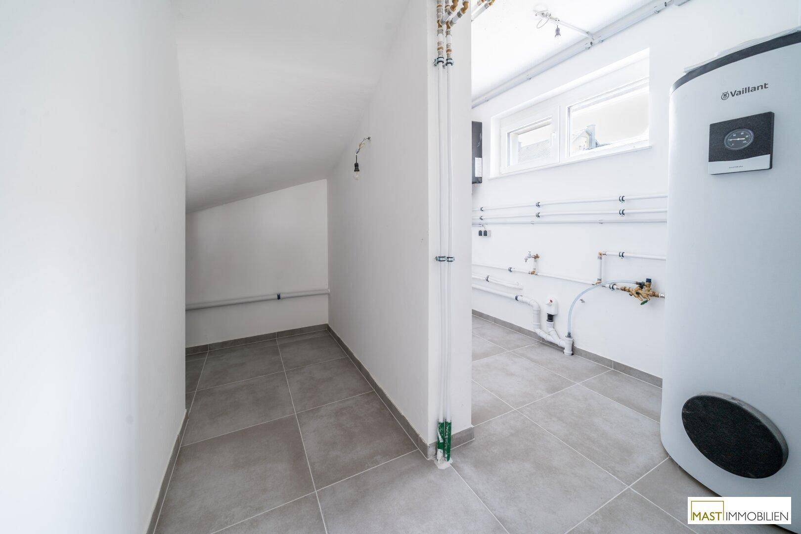 Hauswirtschaftsraum mit Warmwasserbereiter, sichtbaren Leitungen und Fenster.