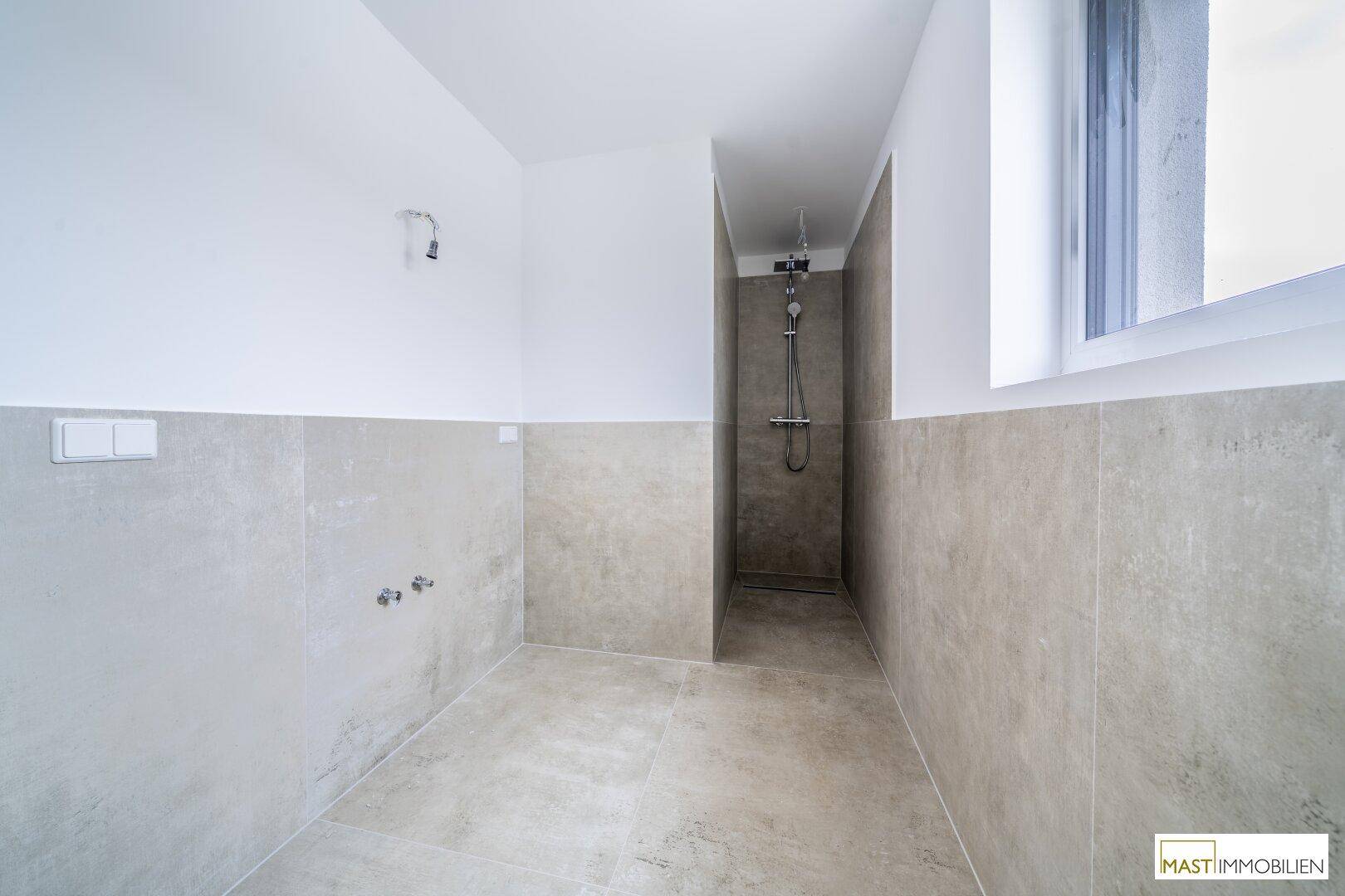 Badezimmer im Bau mit Duschbereich, Fliesenboden und Fenster für Tageslicht.