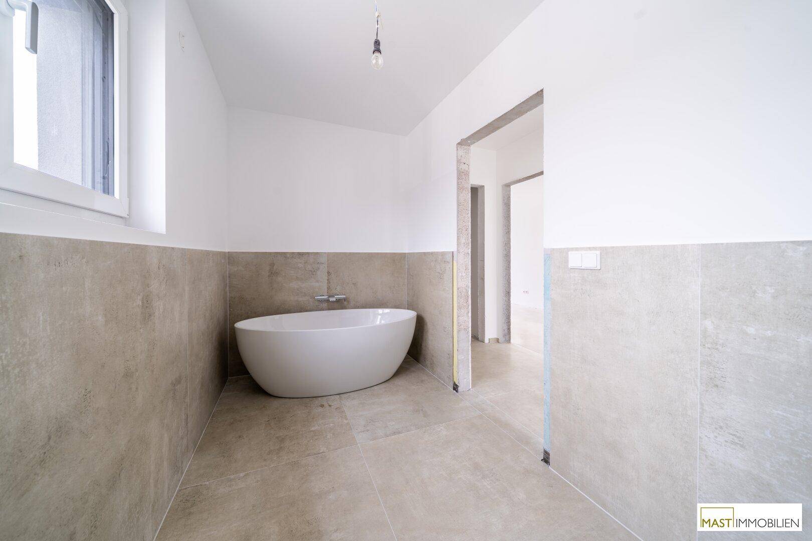 Geräumiges Badezimmer im Bau mit freistehender Badewanne, Fliesen und Fenster.