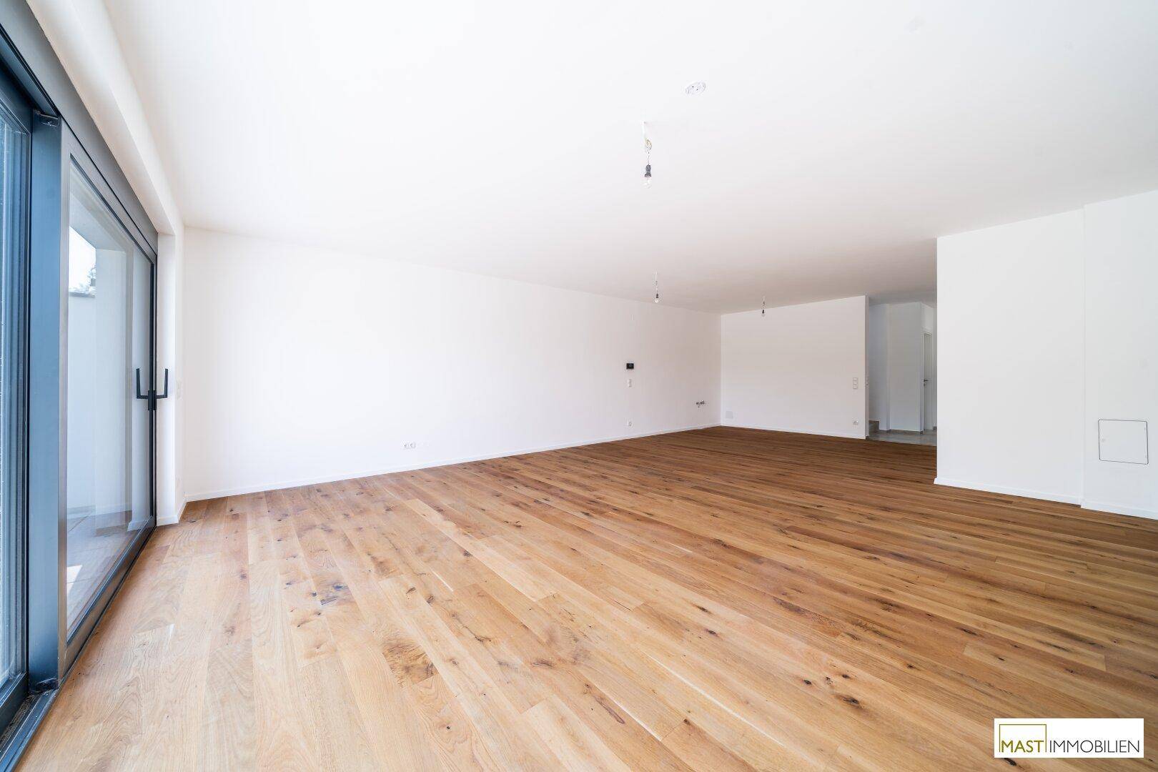 Weitläufiges Wohnzimmer mit Eichenparkett und Schiebetür zum Außenbereich, ideal für offenes Wohnen.