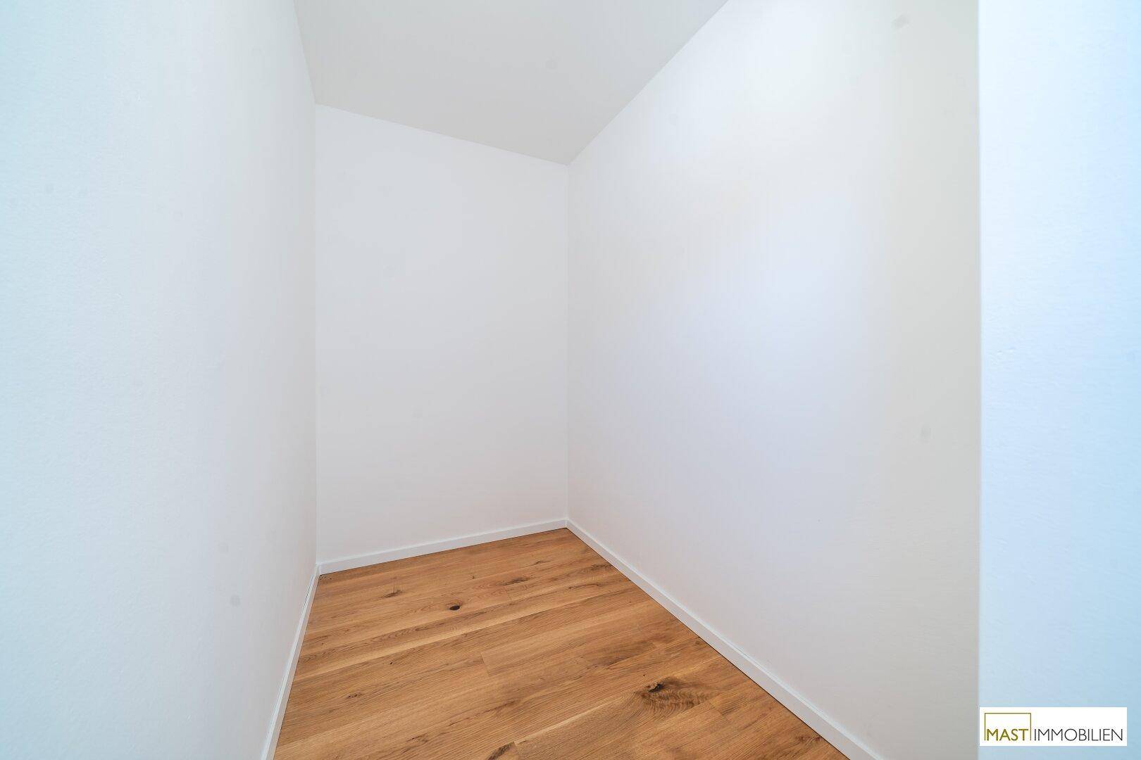 Kleiner, heller Raum mit Holzboden und weißen Wänden, ideal als Abstellraum oder Ankleidezimmer.