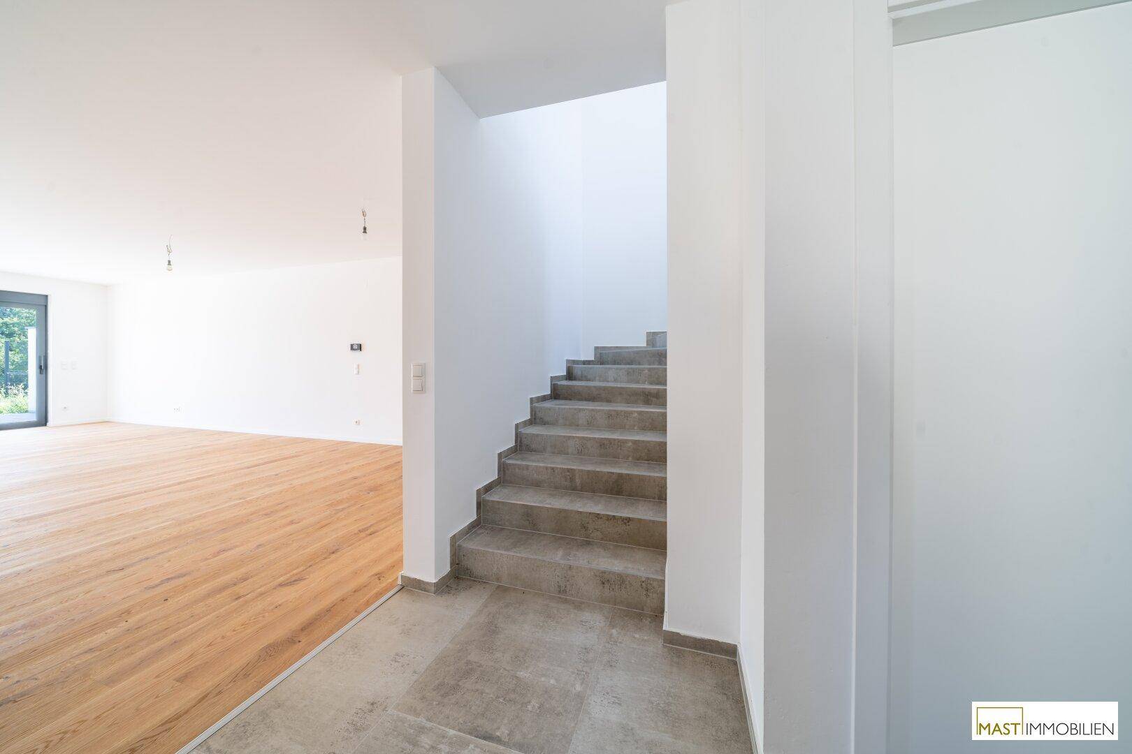 Übergangsbereich mit Fliesenboden, der zu einem hellen Wohnbereich mit Holzparkett und einer Treppe führt.