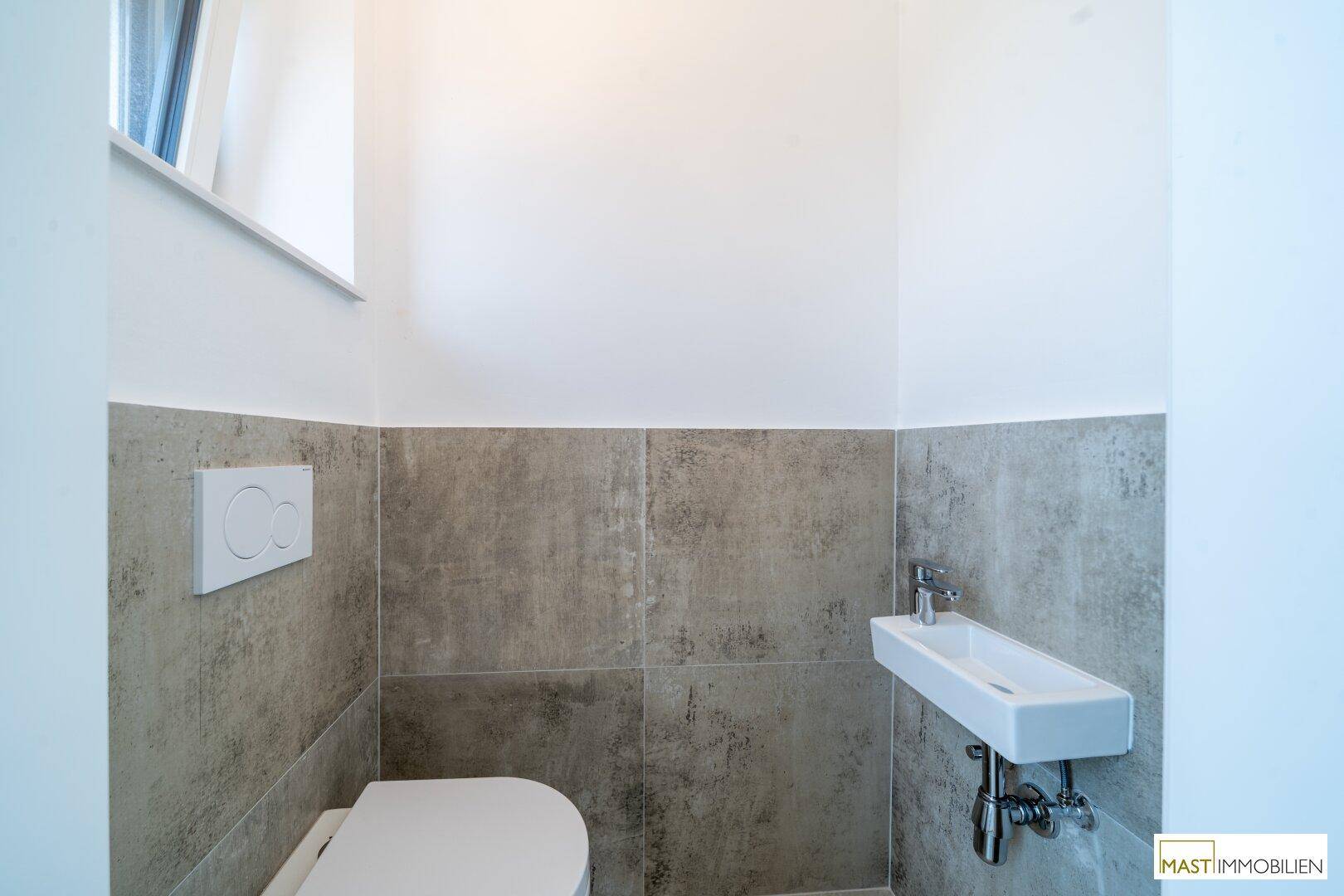 Kleines Gäste-WC mit wandhängender Toilette, kompaktem Waschbecken und Fenster für Belüftung.