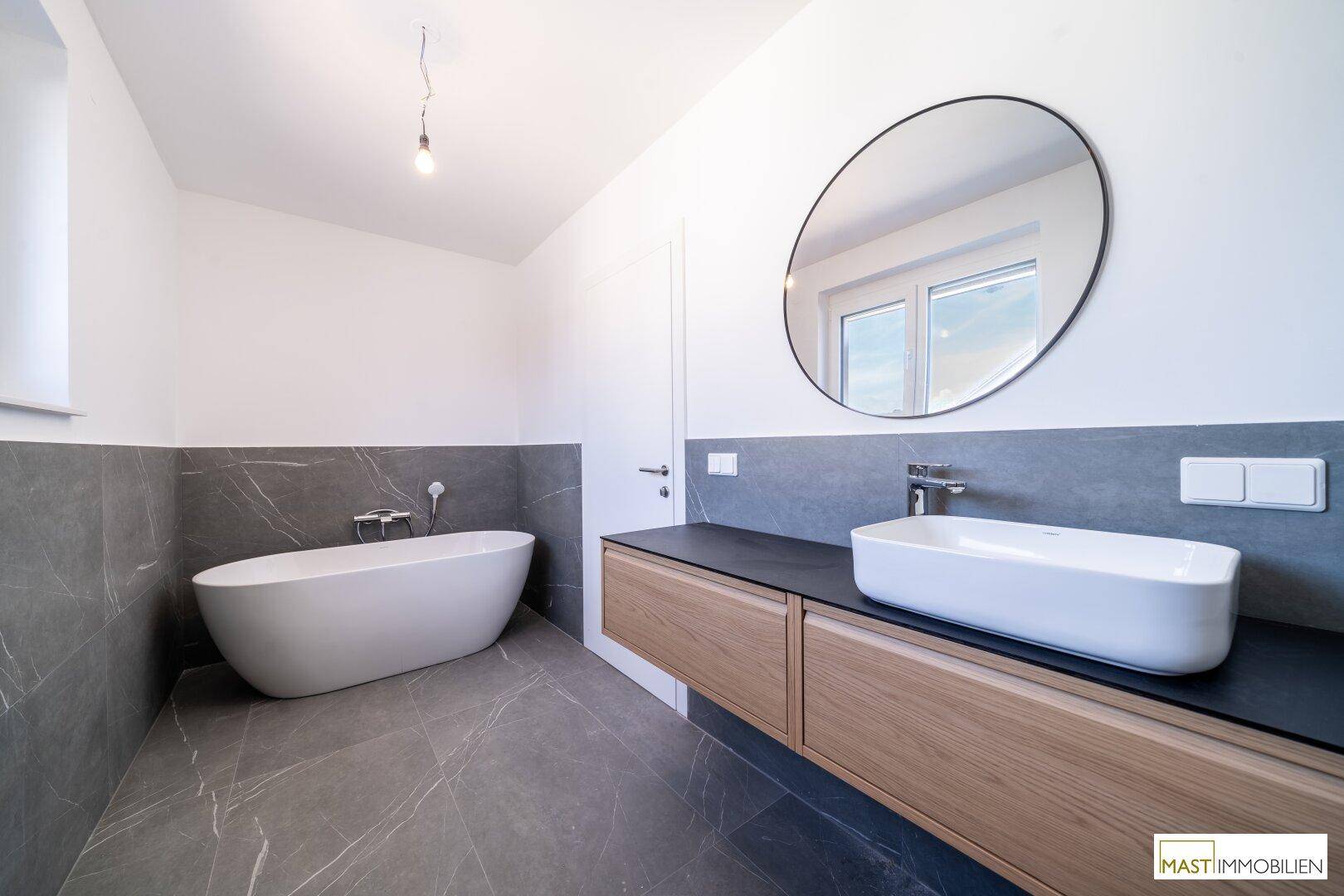Großes Badezimmer mit freistehender Badewanne, modernem Waschtisch und eleganten Marmorfliesen.