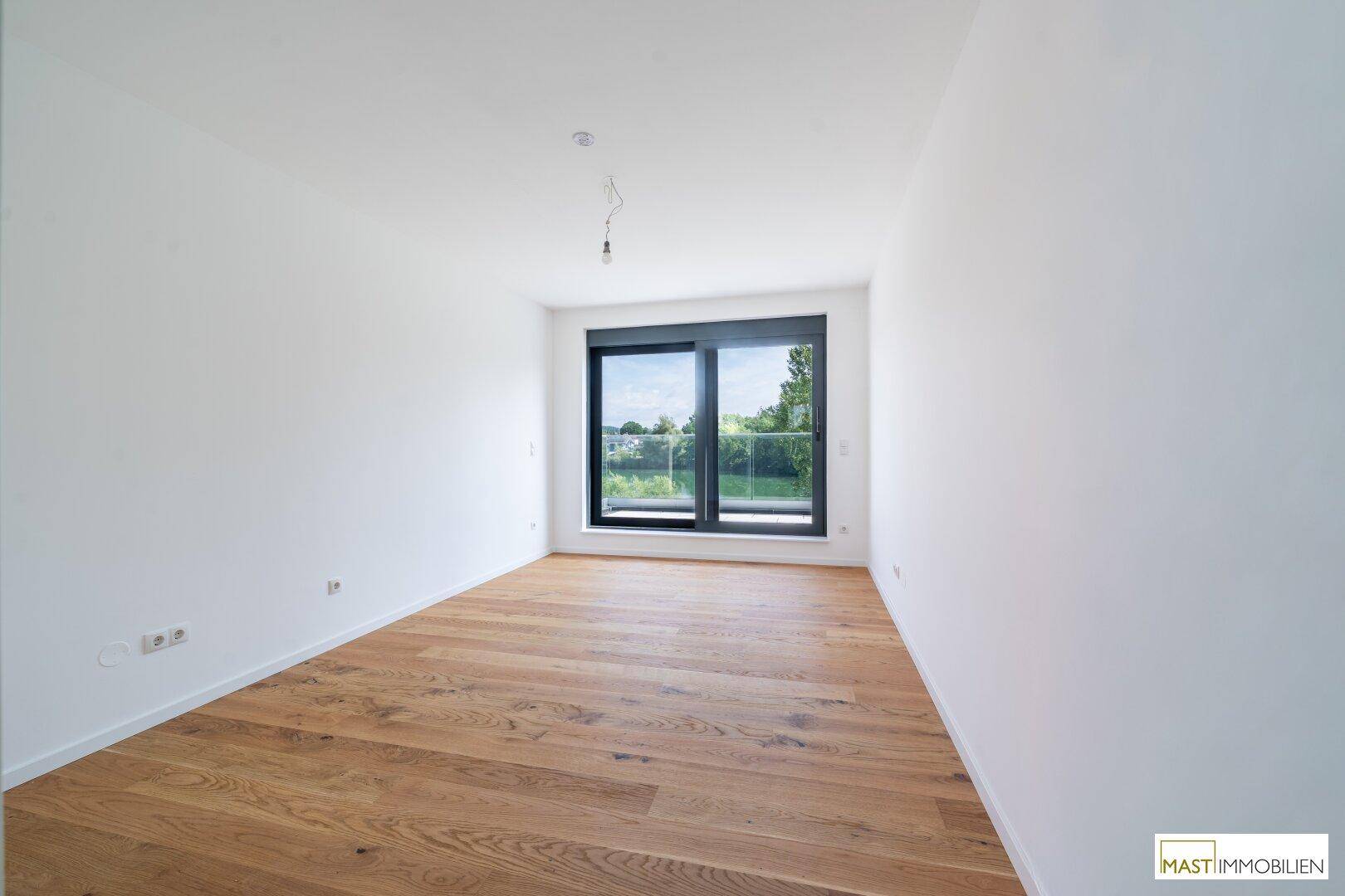 Helles Schlafzimmer mit Eichenparkett und großem Fenster, das einen weiten Blick ins Grüne ermöglicht.