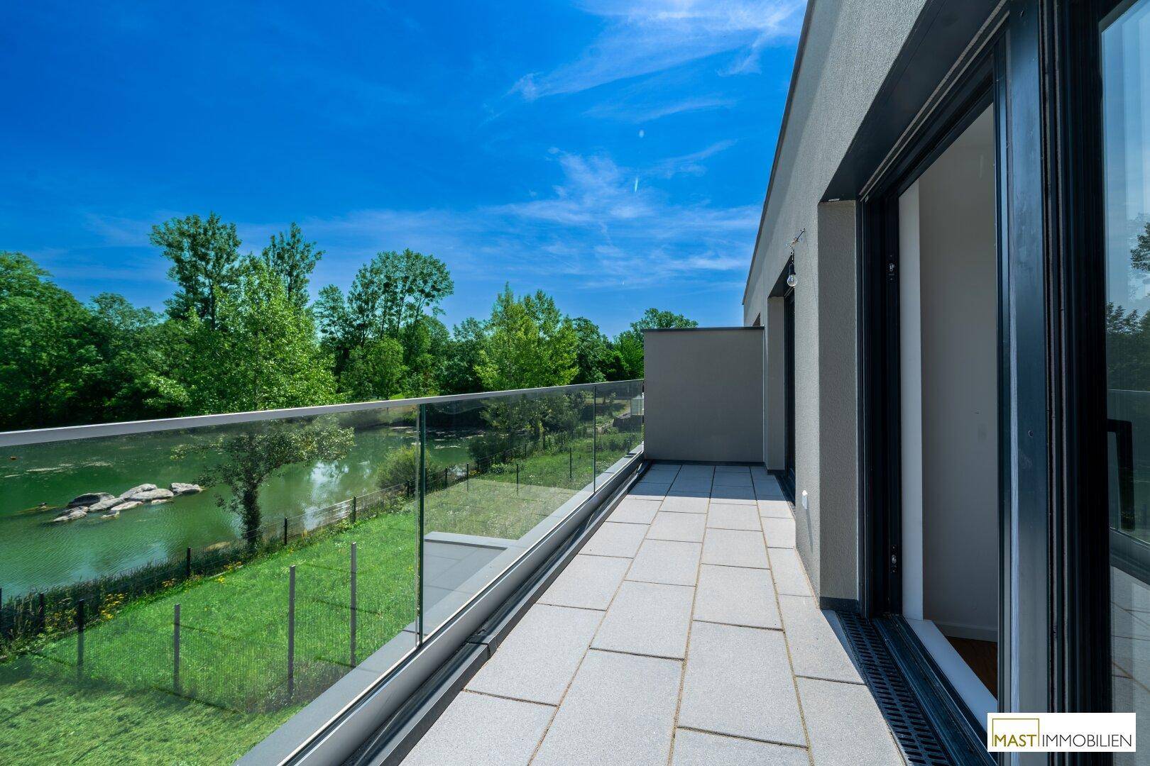 Geräumiger Balkon mit Glasgeländer und atemberaubendem Blick auf den See und die umliegende Natur.